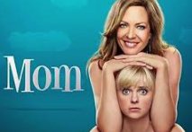 Promotional poster for the movie 'Mom' featuring a smiling woman and a girl with blonde hair against a blue background.