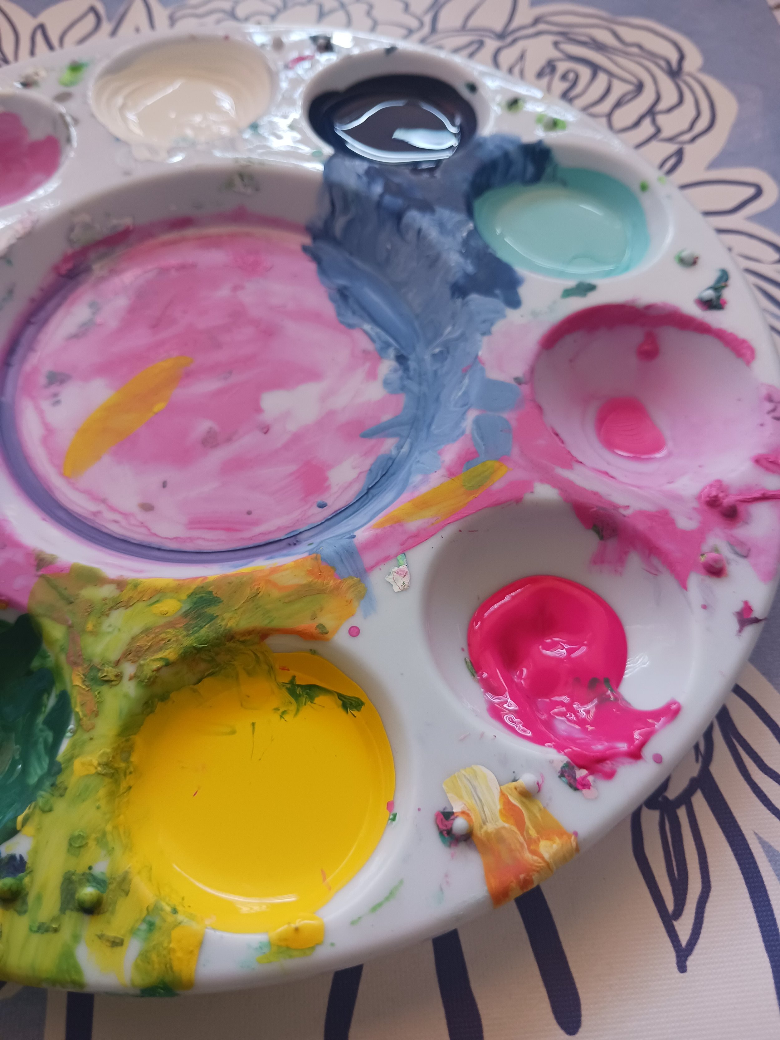 A paint palette with various colors including pink, yellow, green, black, white, and blue, some of which are mixed together.