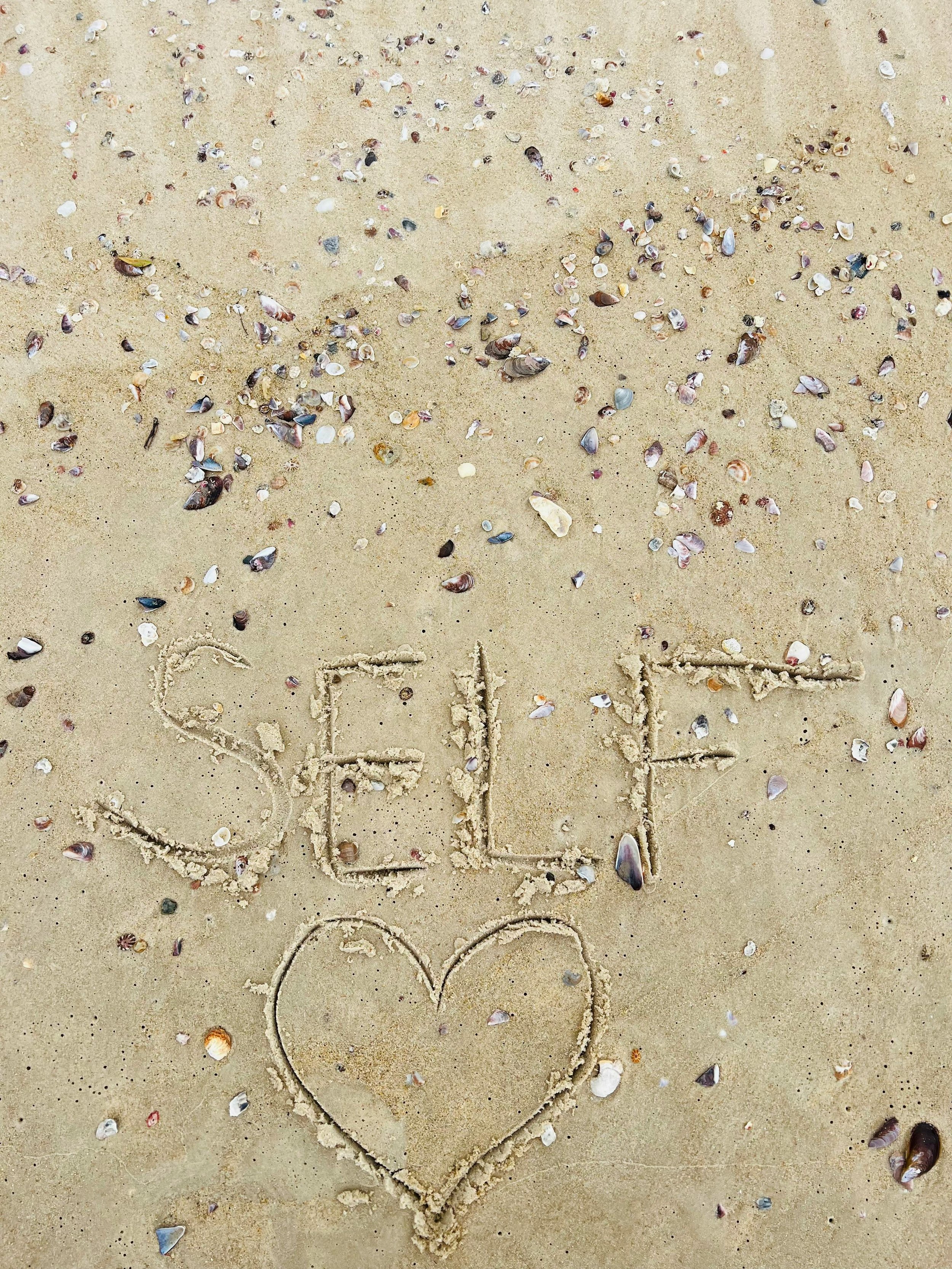 Shells arranged in sand spelling SELF with a heart representing self-compassion and healing in EMDR and IFS therapy for women in NY