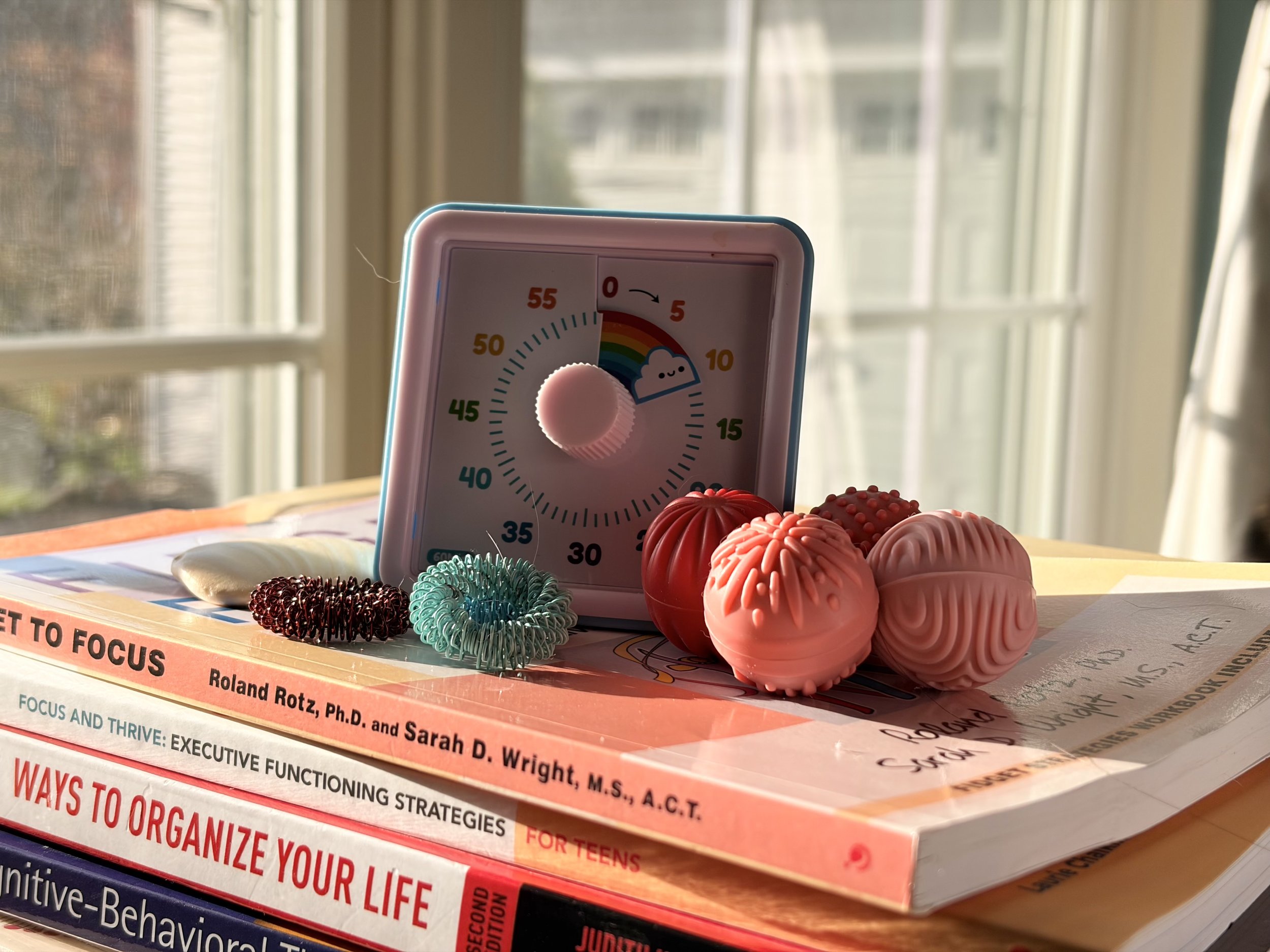 A tabletop with an ADHD timer, sensory fidgets, and a book about organizing life with ADHD, on a therapist's desk