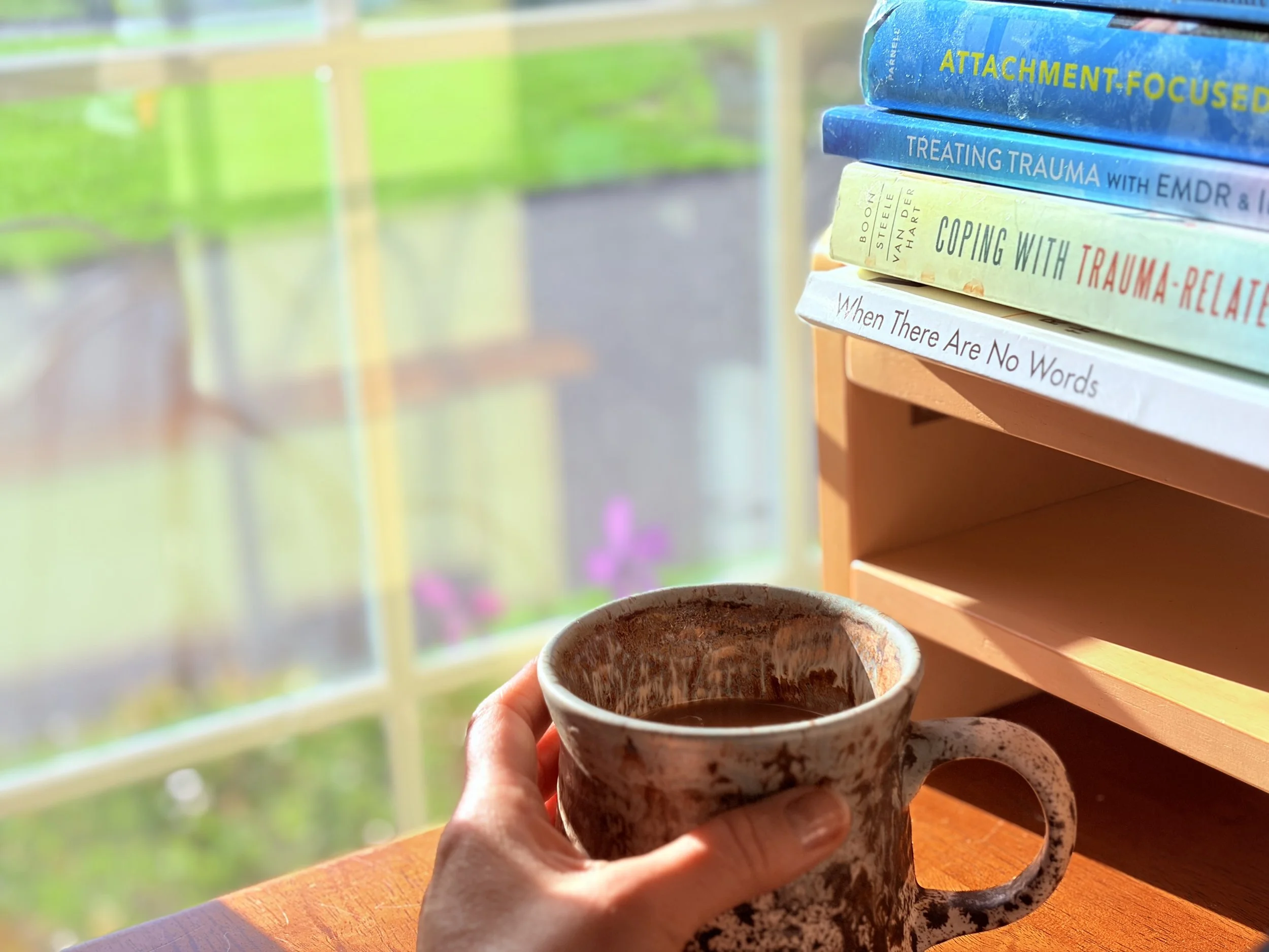 therapist holding coffee cup near books on EMDR, trauma and attachment-focused EMDR by a window with warm morning light