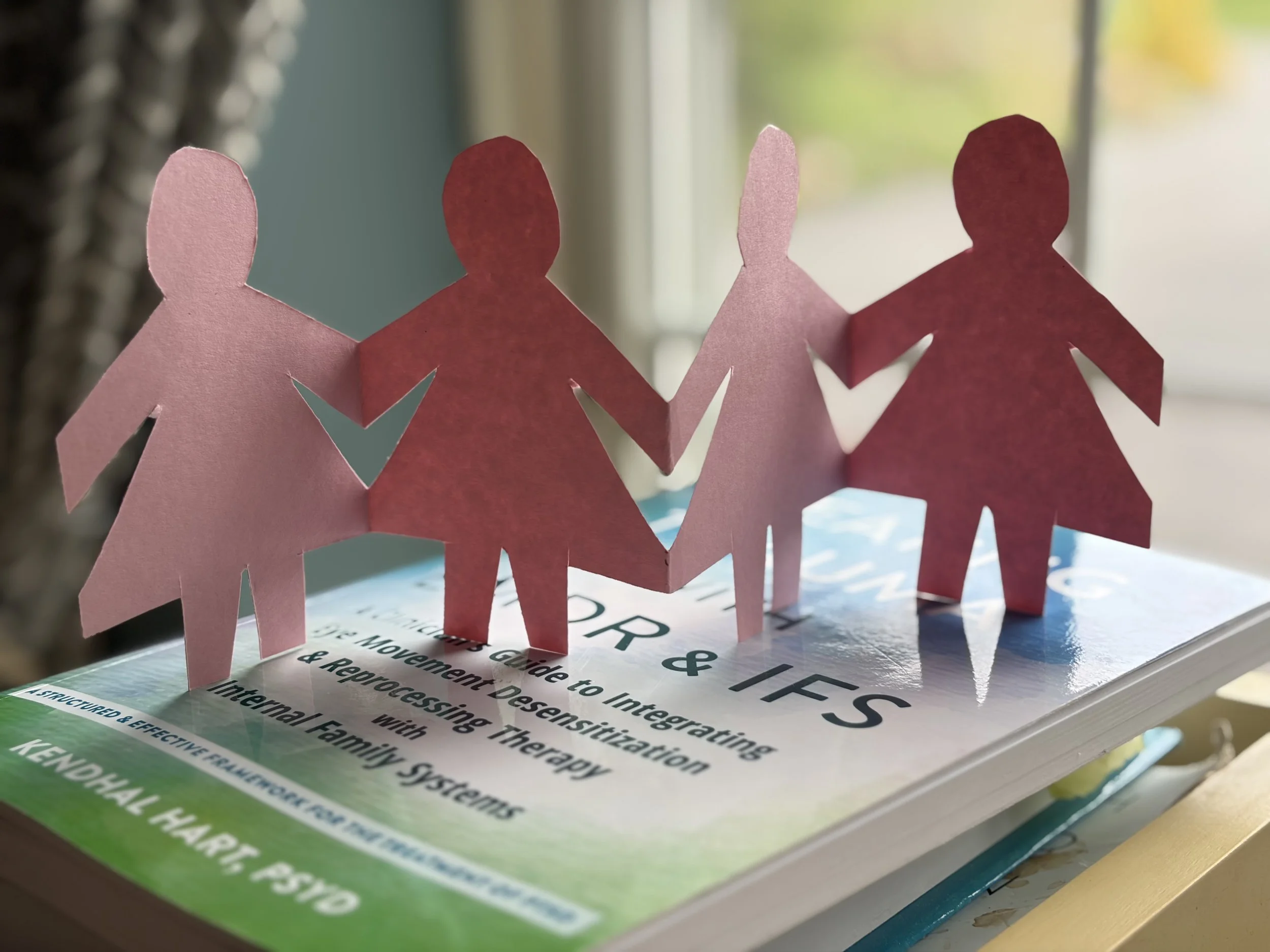 Paper doll figures on EMDR and IFS therapy book representing parts work and internal family systems