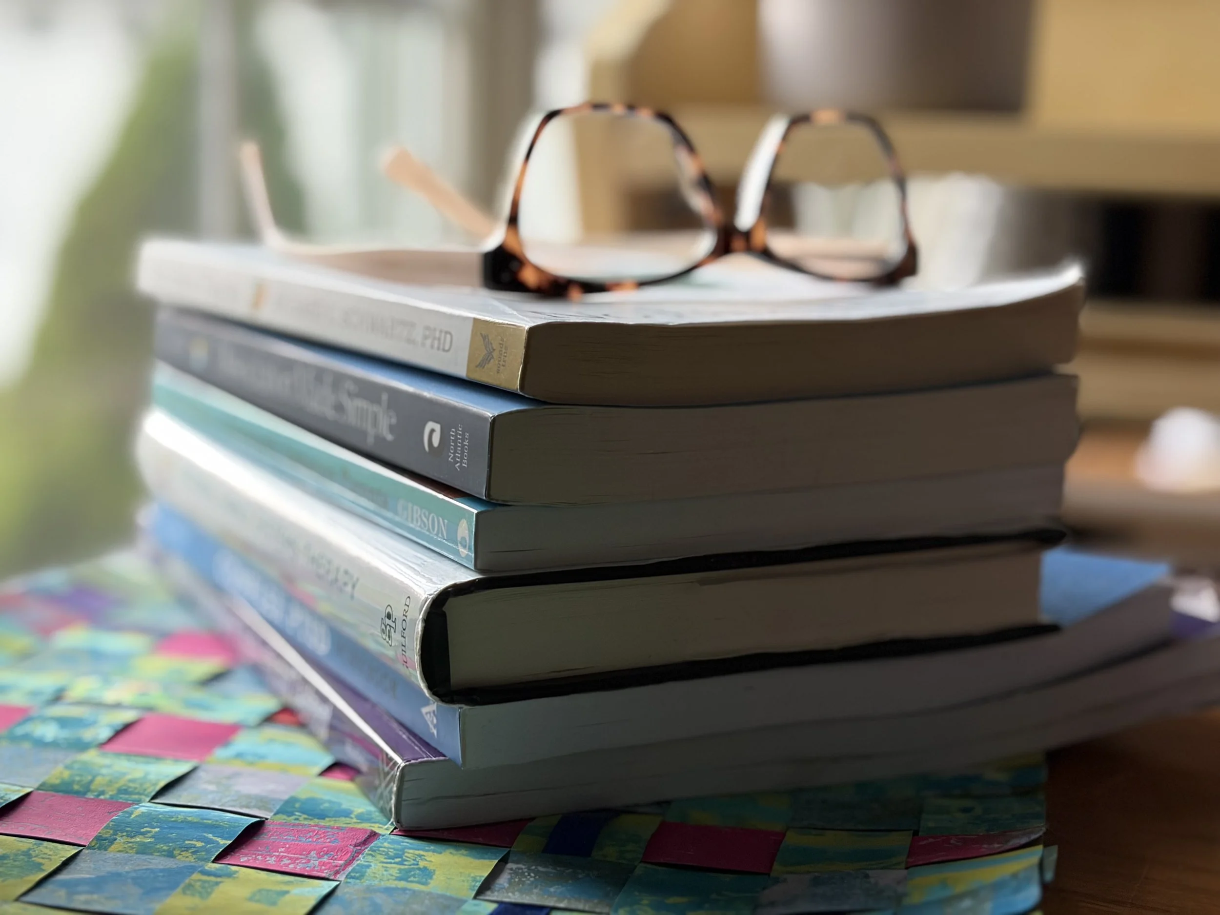 A stack of EMDR, IFS, and attachment books with glasses on a therapist's desk
