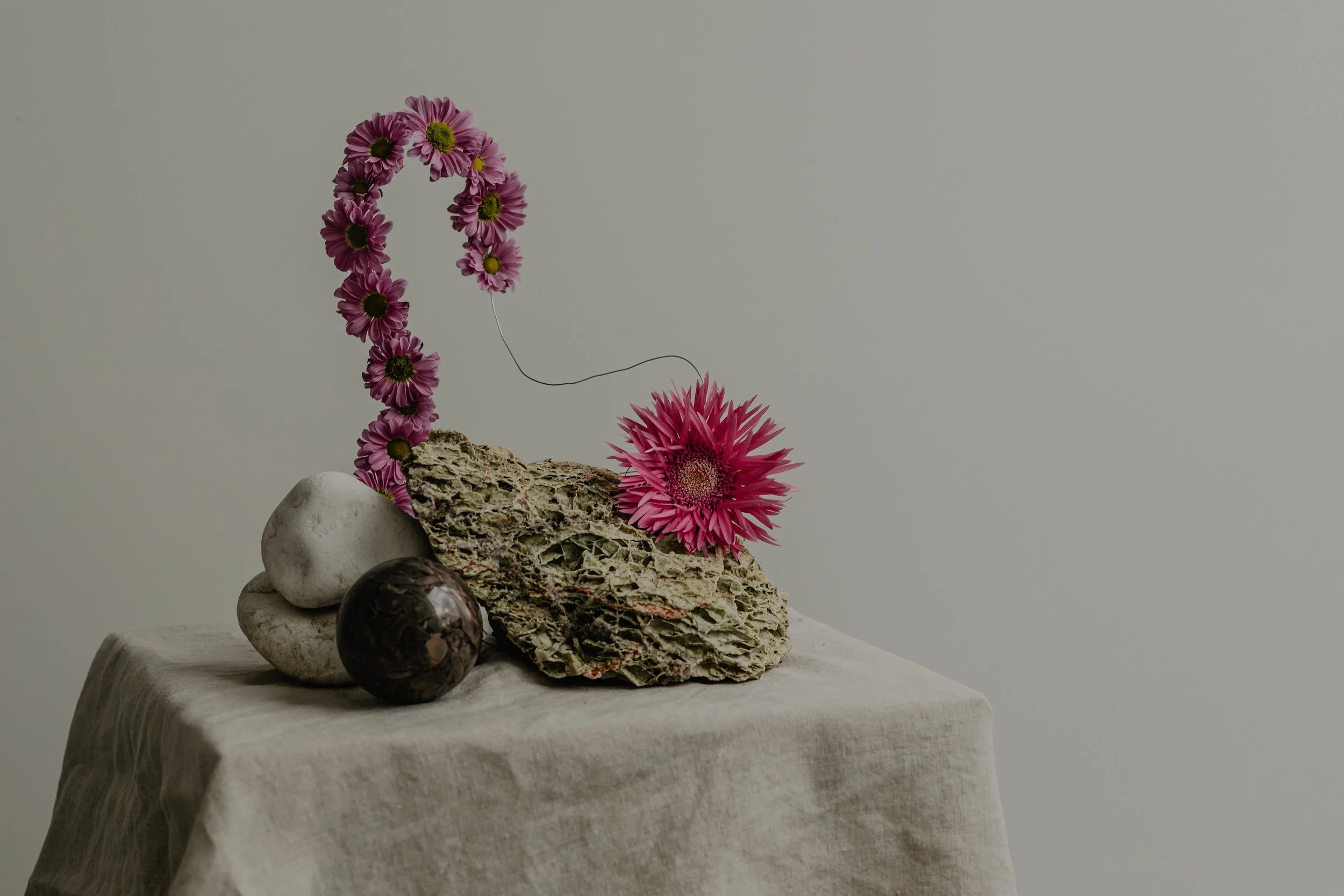 Arrangement of decorative stones, a piece of textured rock, and pink flowers on a white cloth-covered surface.