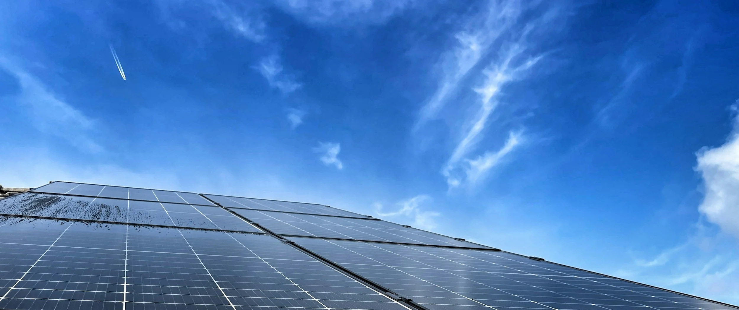 Solar panels on a roof with a bright blue sky and wispy clouds above.
