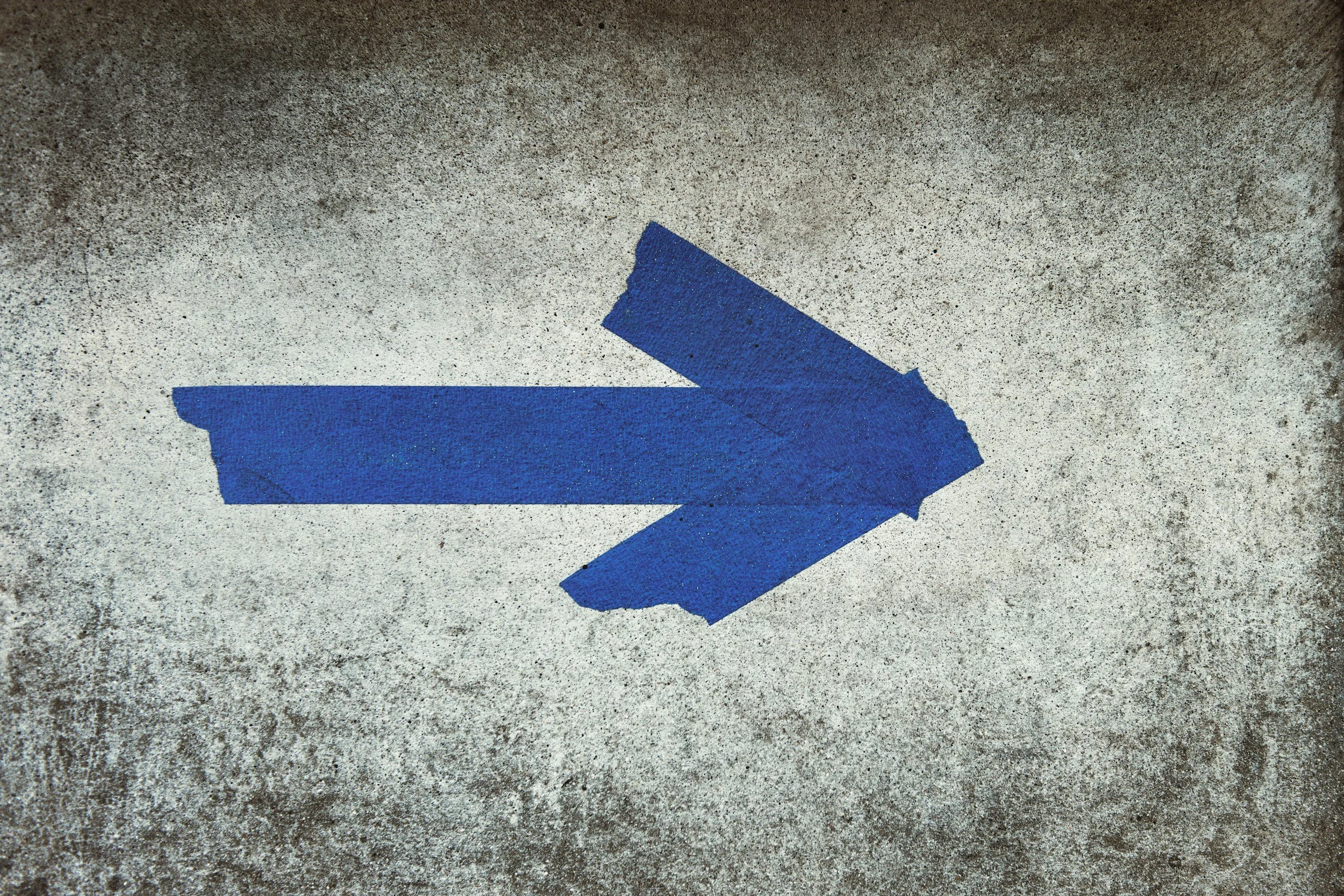Blue painted arrow pointing to the right on a concrete surface.