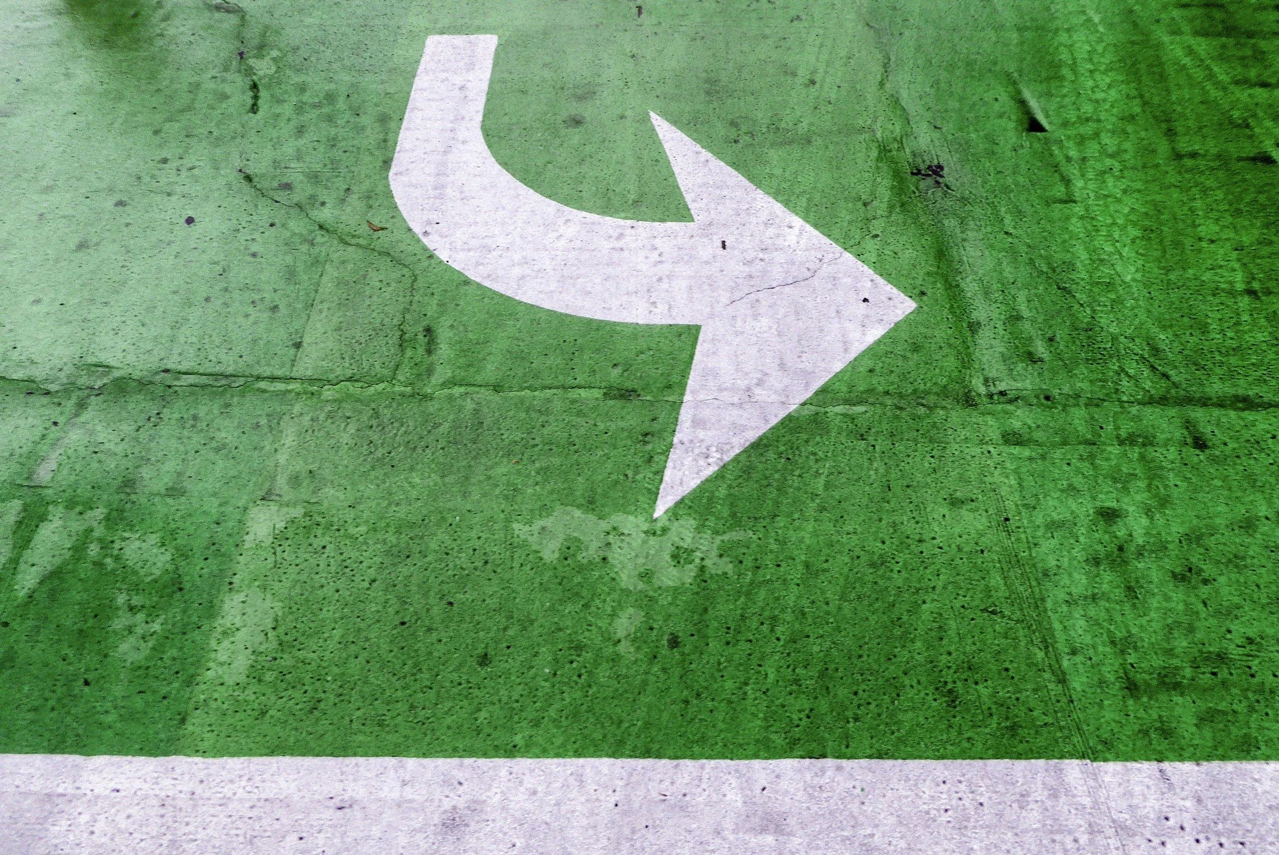 Green pavement with a white directional arrow pointing to the right.