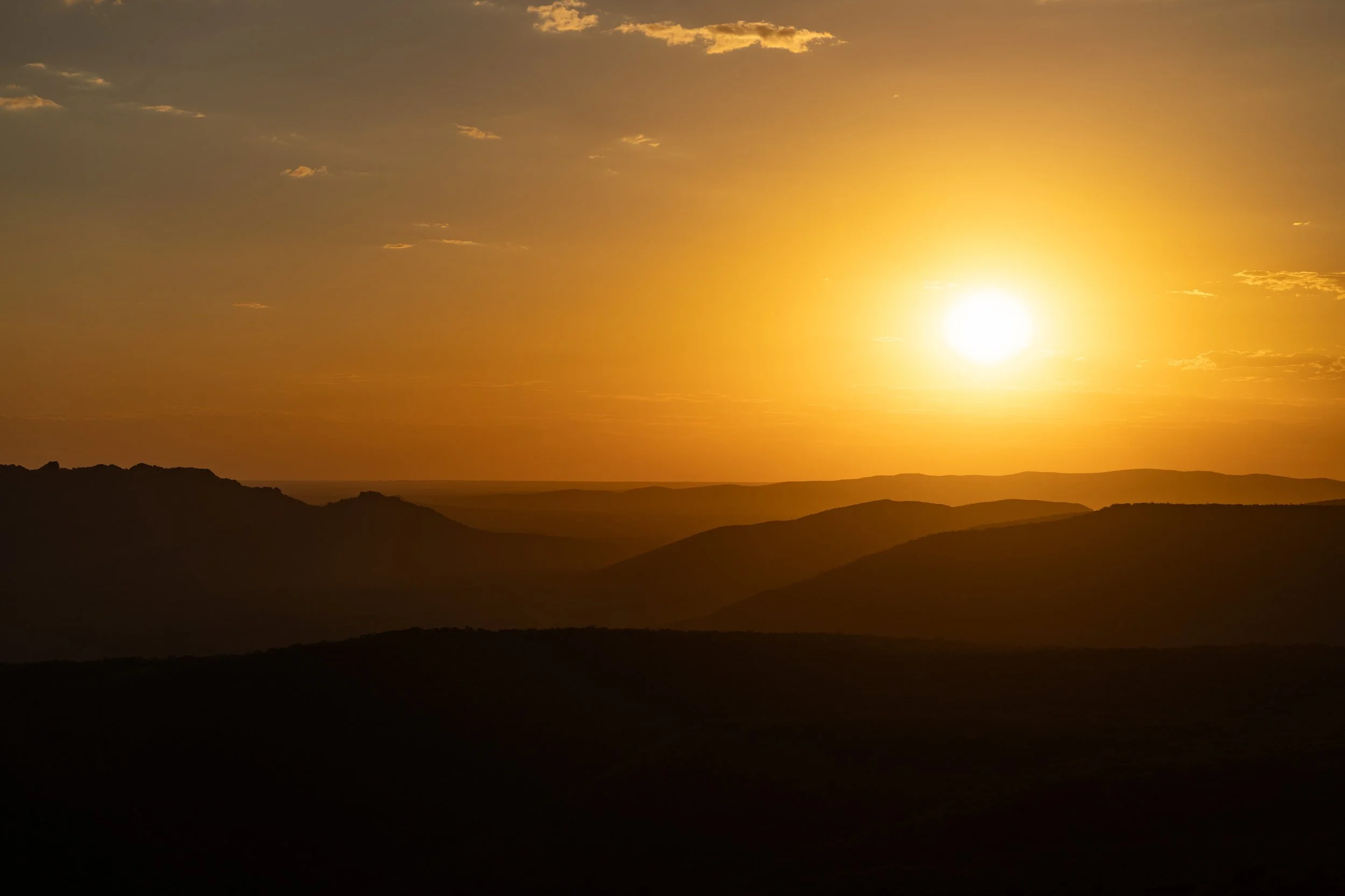Sunset over mountains, with a golden sky and a few clouds.