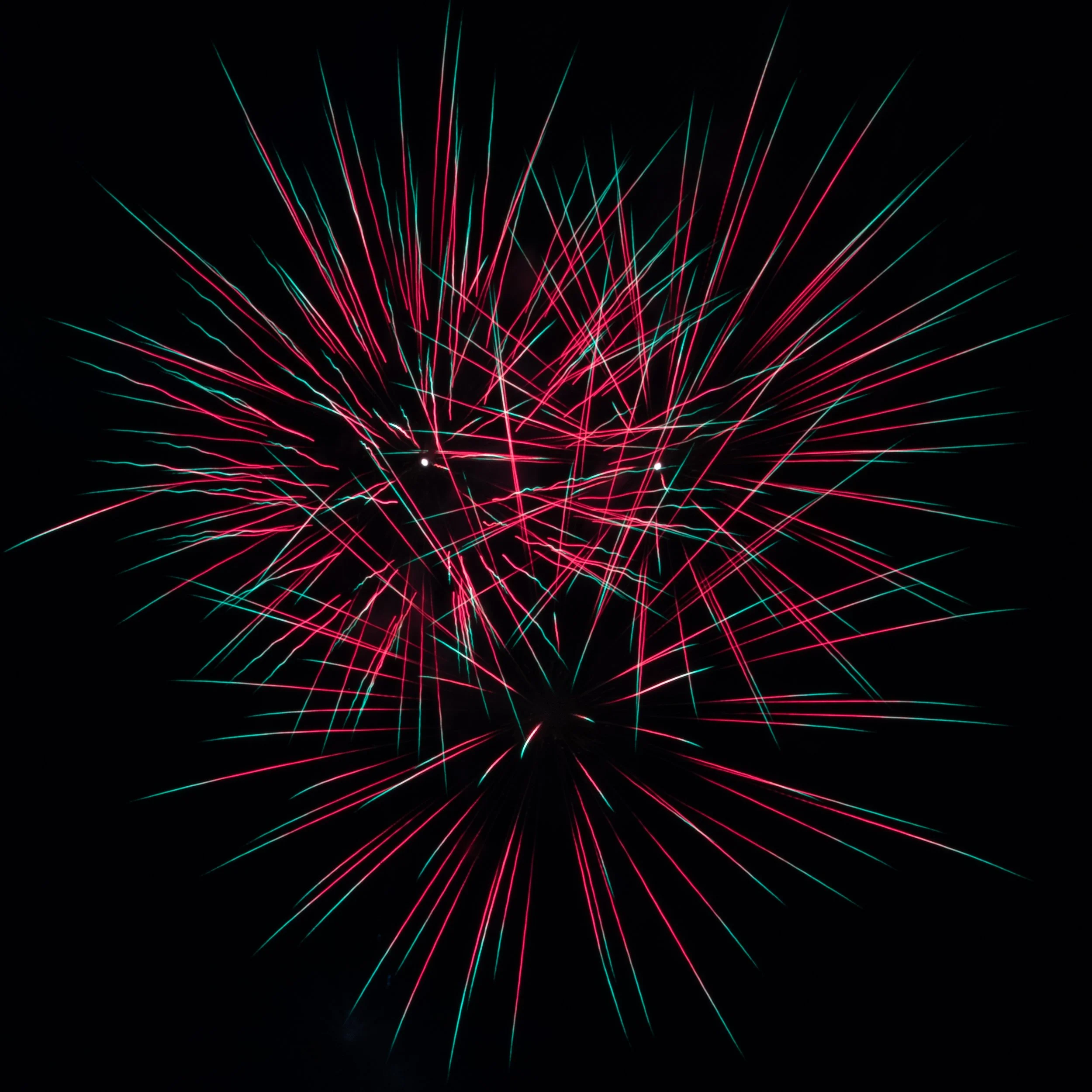 Colorful fireworks exploding against a black night sky with red and teal streaks.