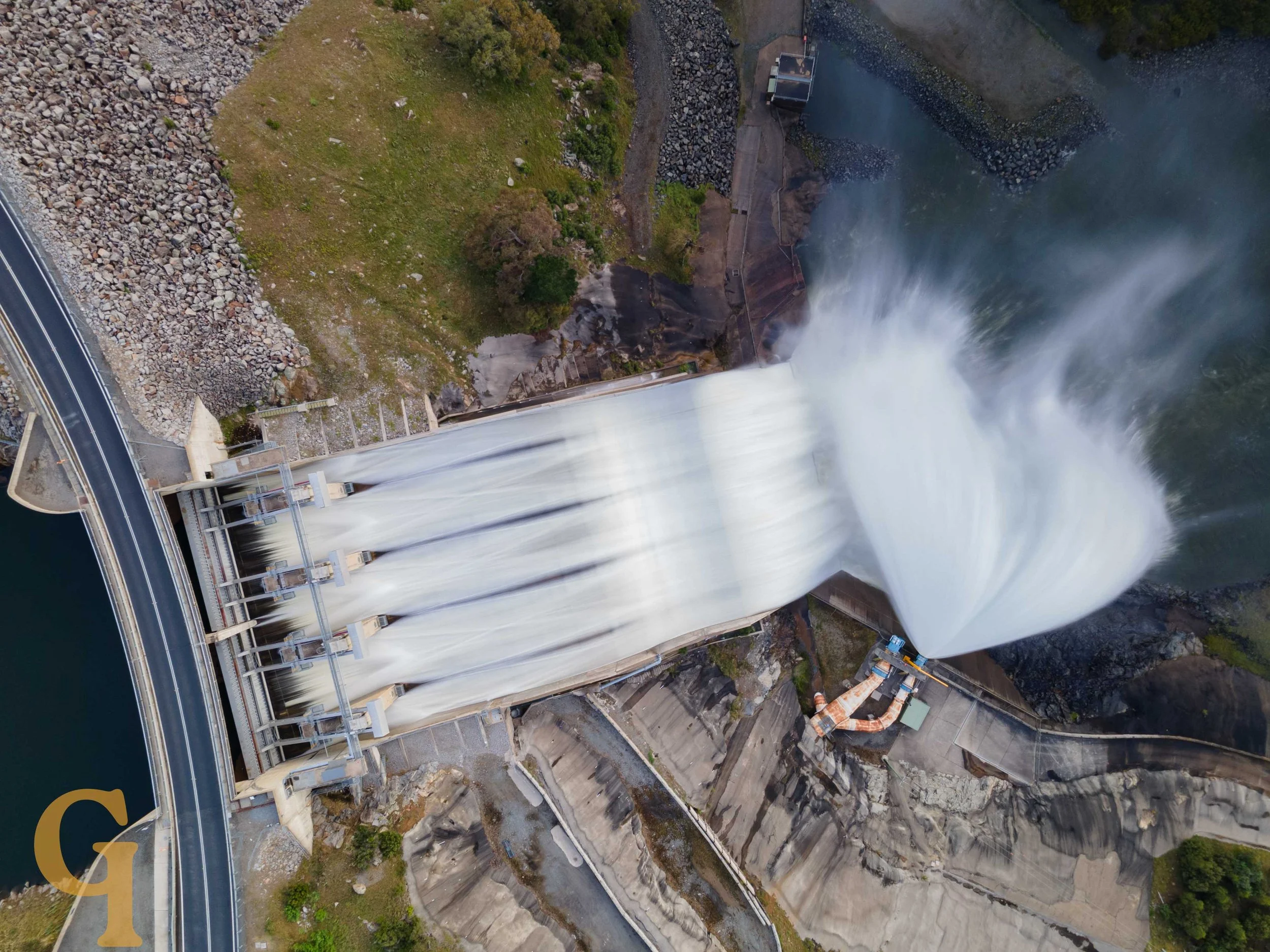 Aerial view of a dam with water flowing over the spillway.