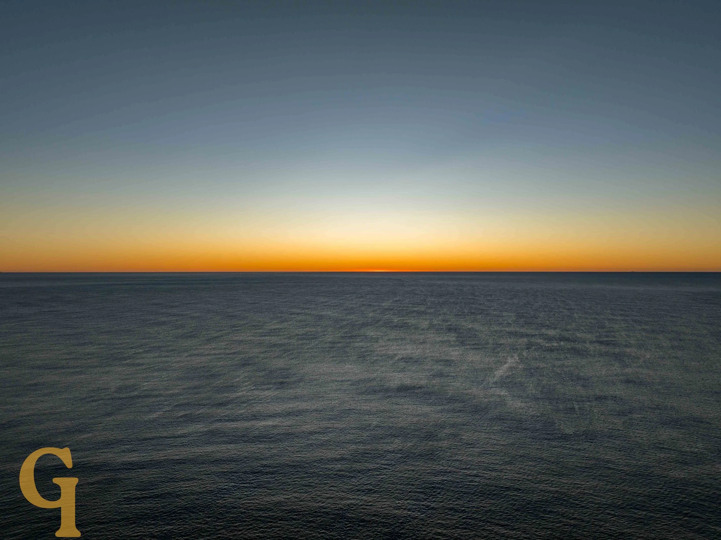 A calm ocean under a rising sun with a clear sky.