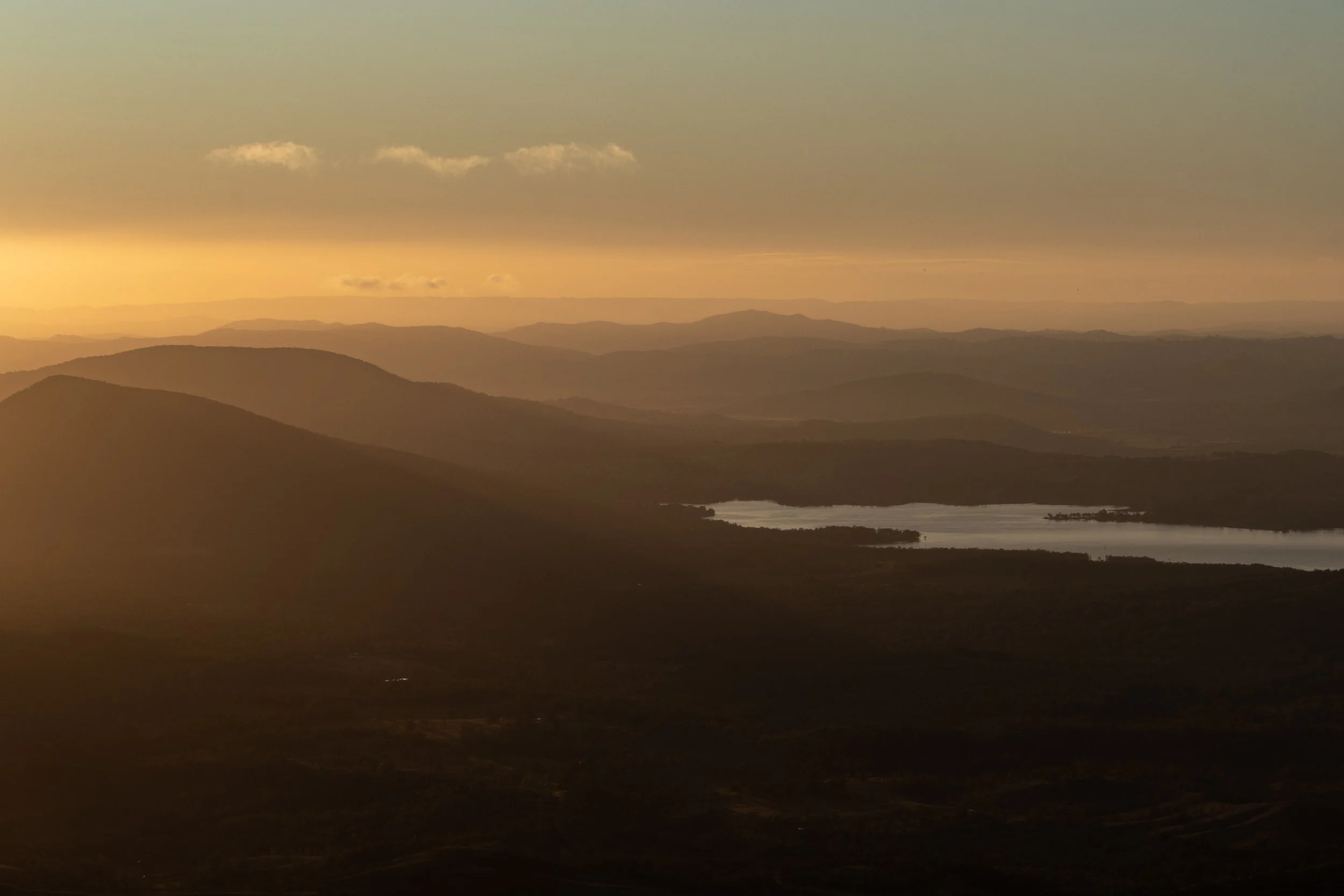Sunset over rolling hills and a lake in the distance.