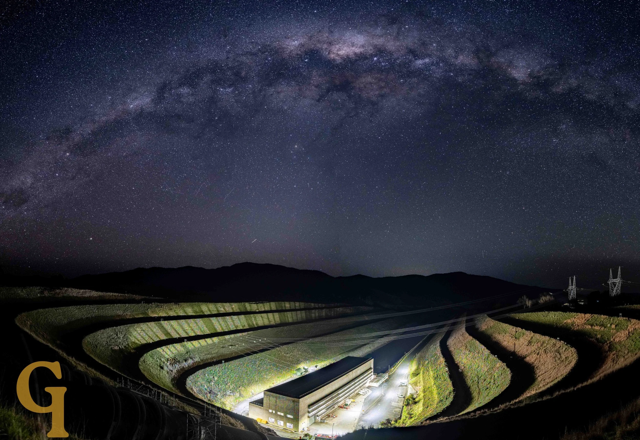 Nighttime landscape of terraced farming fields with a building at the bottom and the Milky Way galaxy visible in the star-filled sky above.
