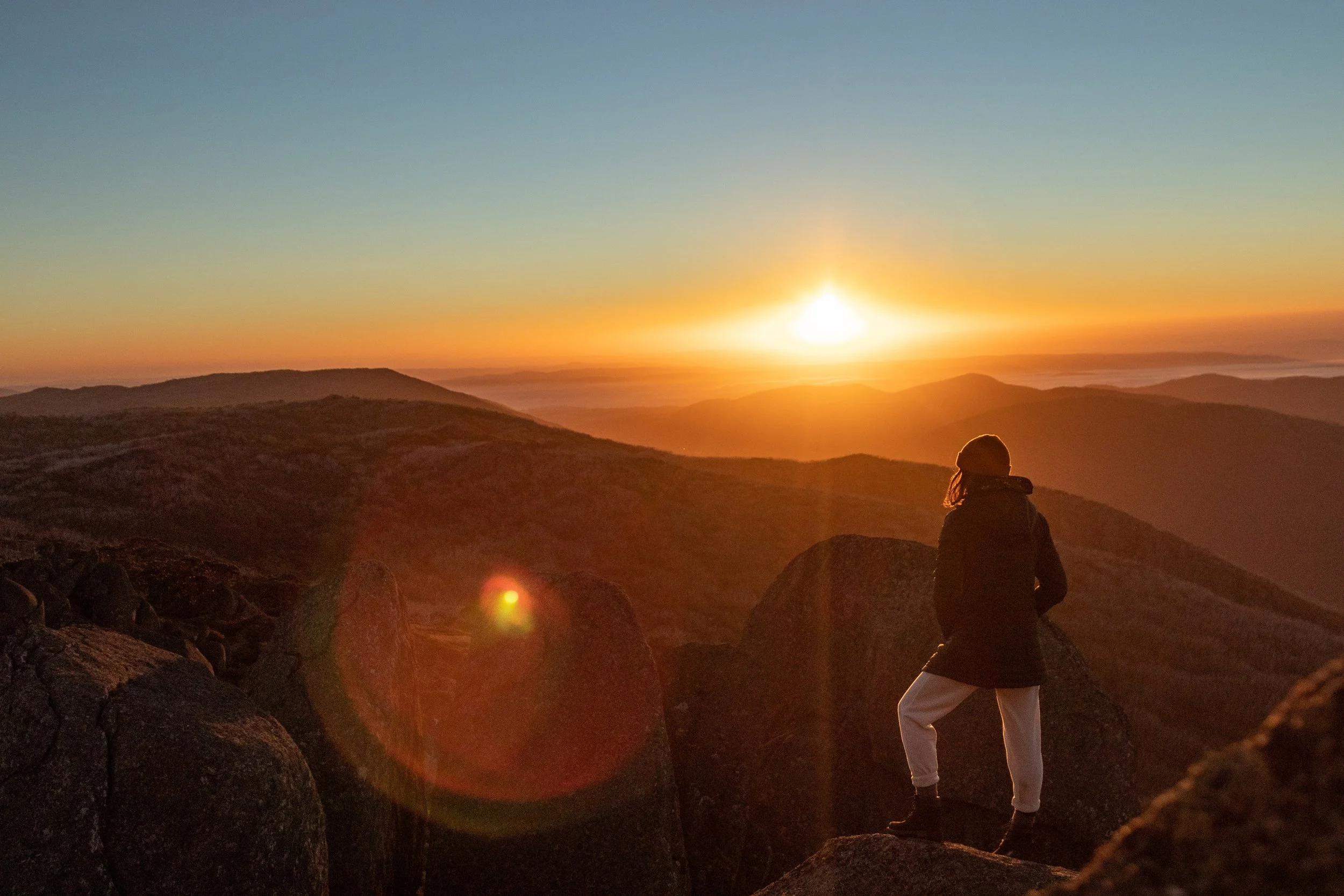 A person standing on rocks during sunset mountain view