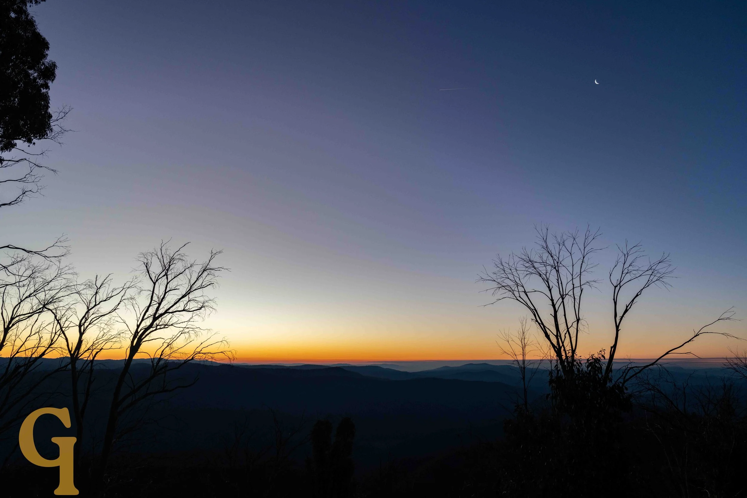 A landscape scene at dusk with a dark sky, a narrow crescent moon, a faint star, and a streak of light. Silhouettes of leafless trees are in the foreground, and distant mountains are visible on the horizon.