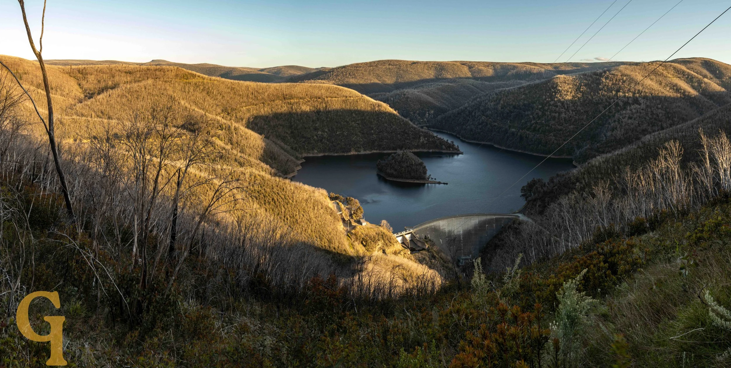 Lake surrounded by forested hills with a dam structure at the foreground.