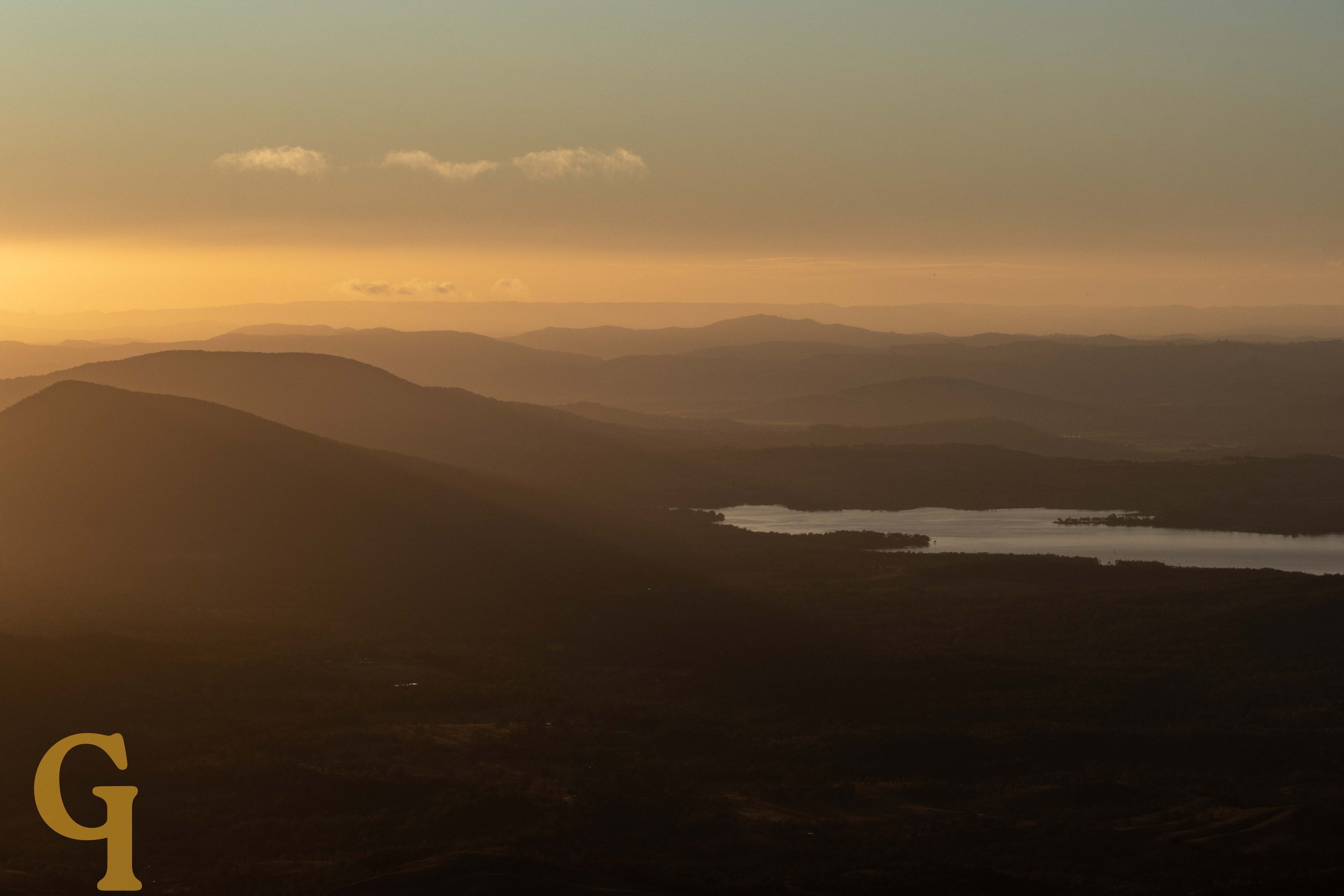 Sunset over rolling hills and a lake in the distance.