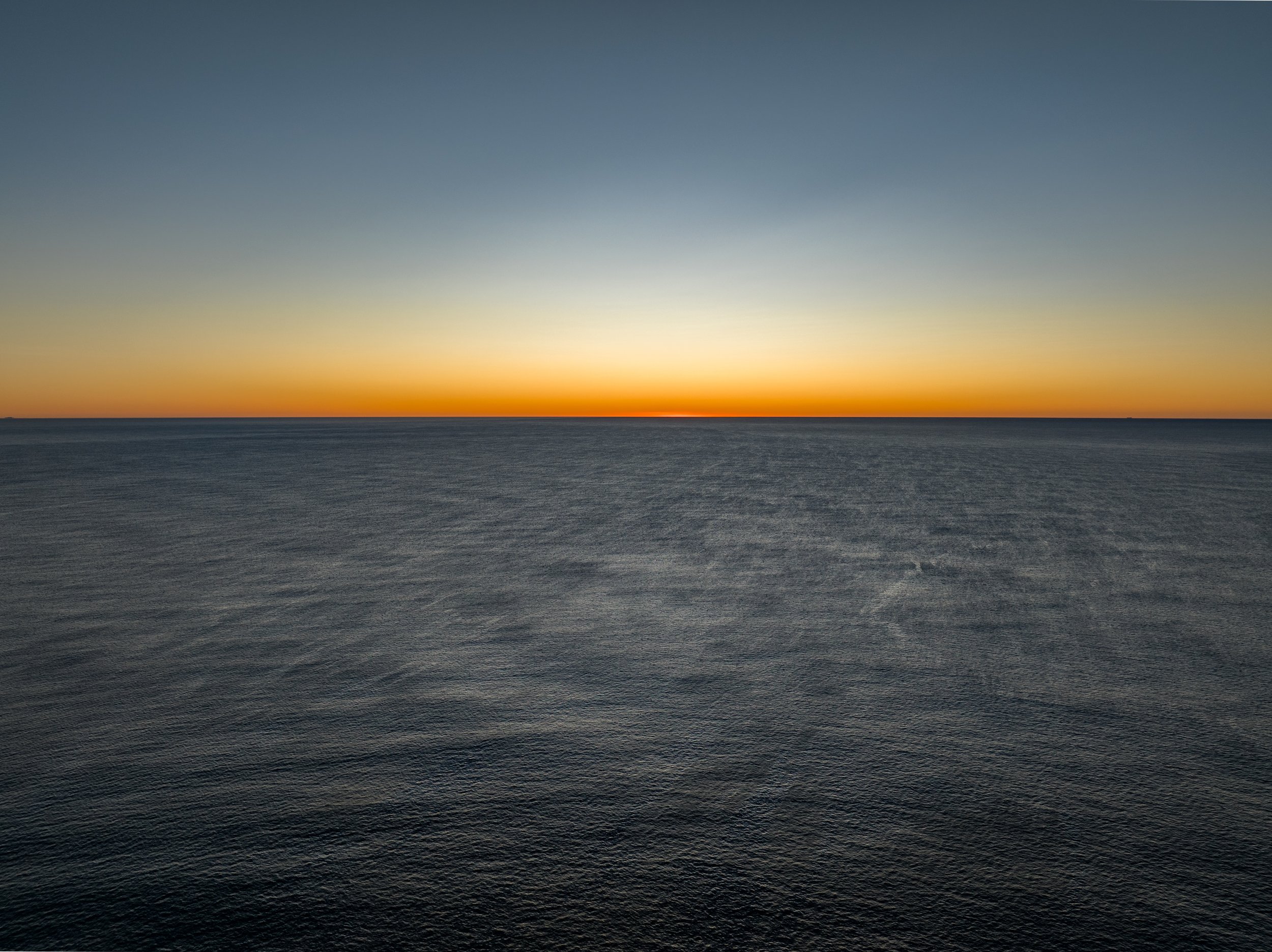 A calm ocean under a setting or rising sun with a clear sky.