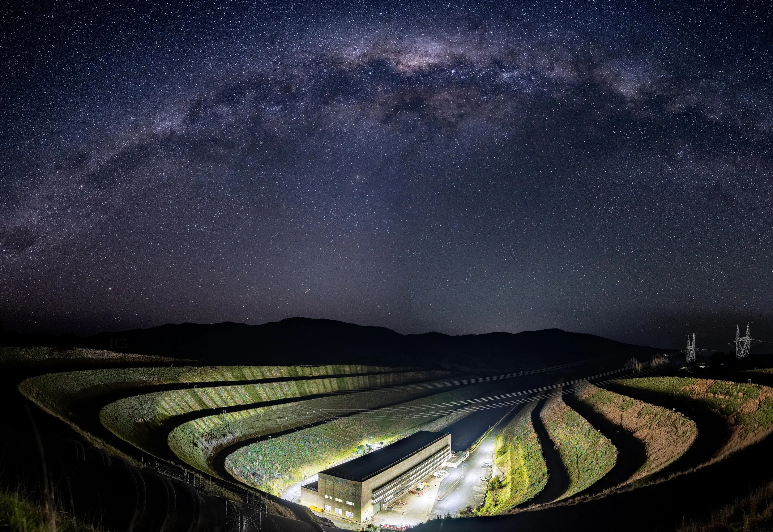 Nighttime landscape of terraced farming fields with a building at the bottom and the Milky Way galaxy visible in the star-filled sky above.