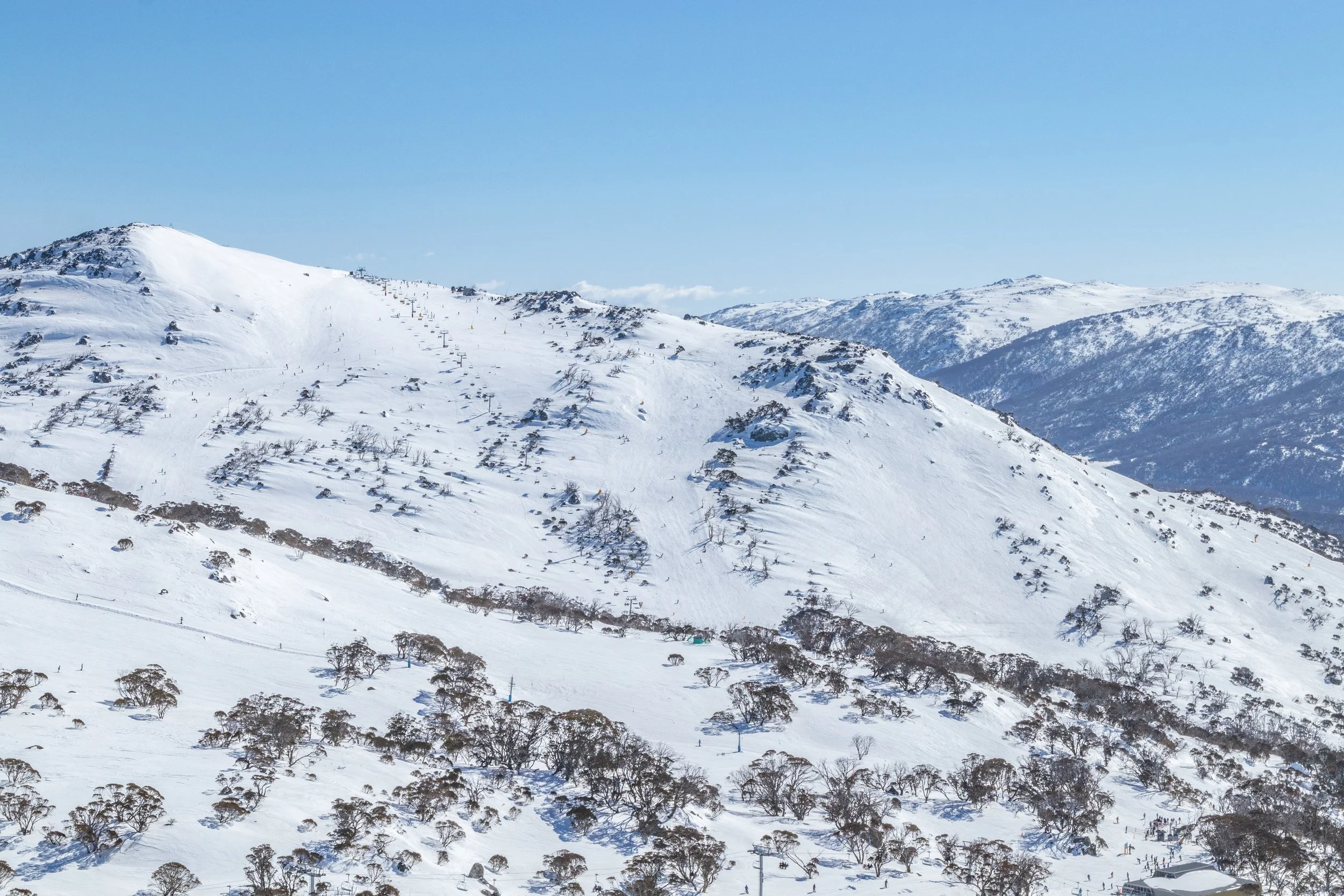 Snow-covered mountain landscape with ski slopes, ski lifts, and sparse trees.