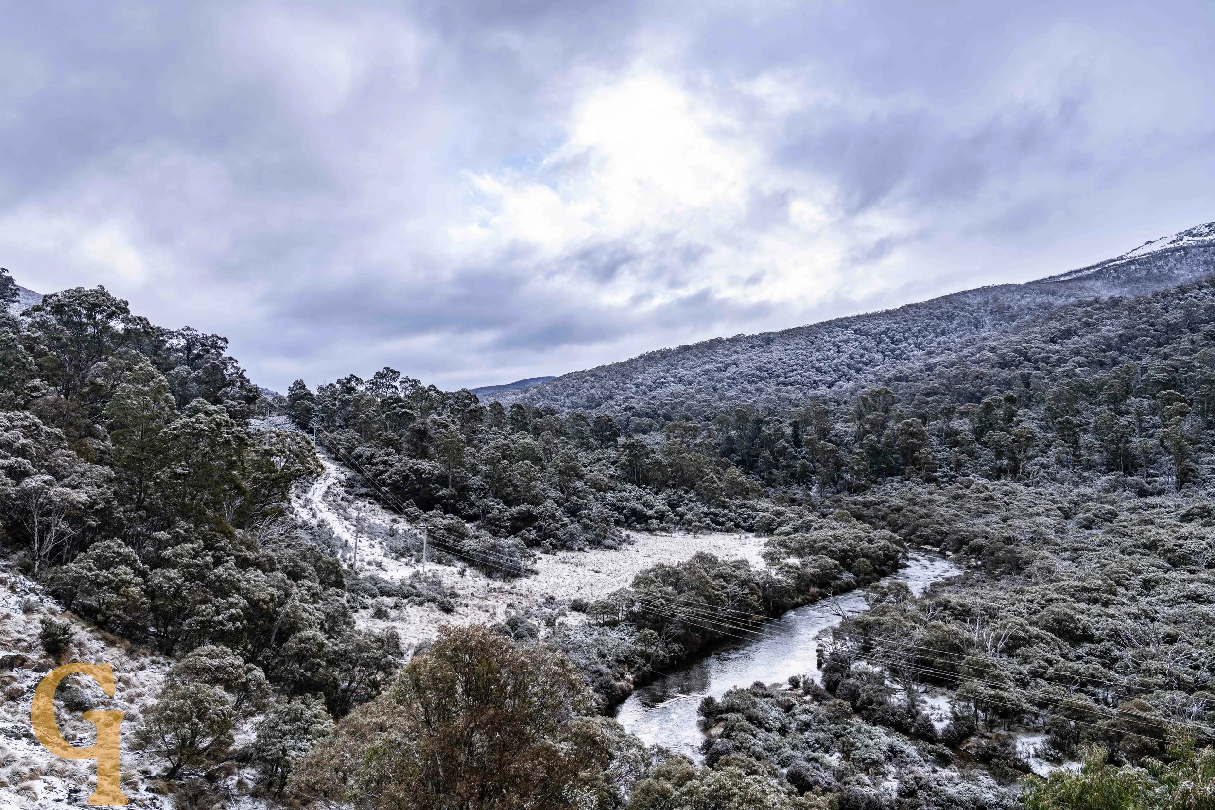 Snow-covered trees and hills surrounding a winding river under a cloudy sky.