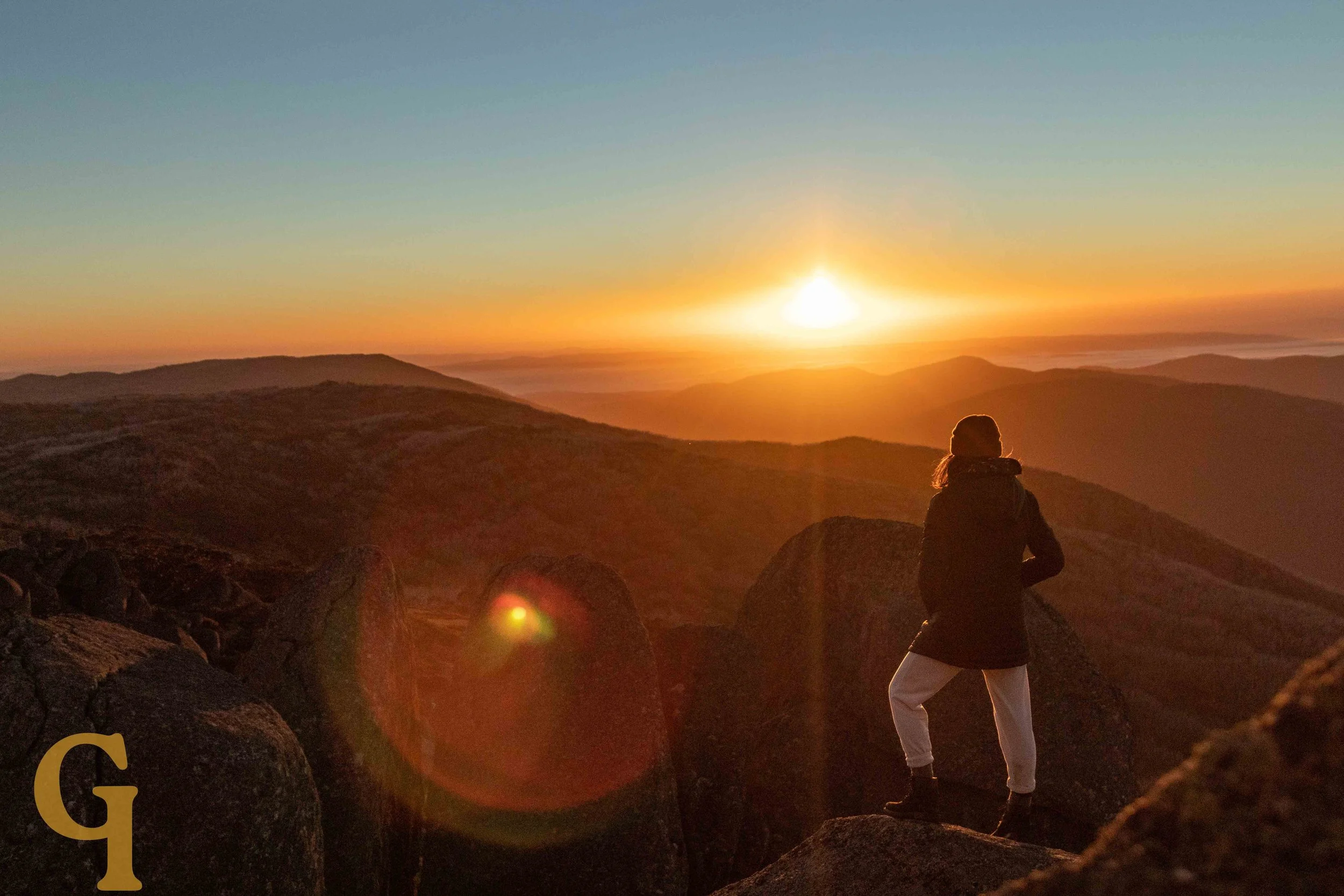 A person standing on rocks during sunrise mountain view