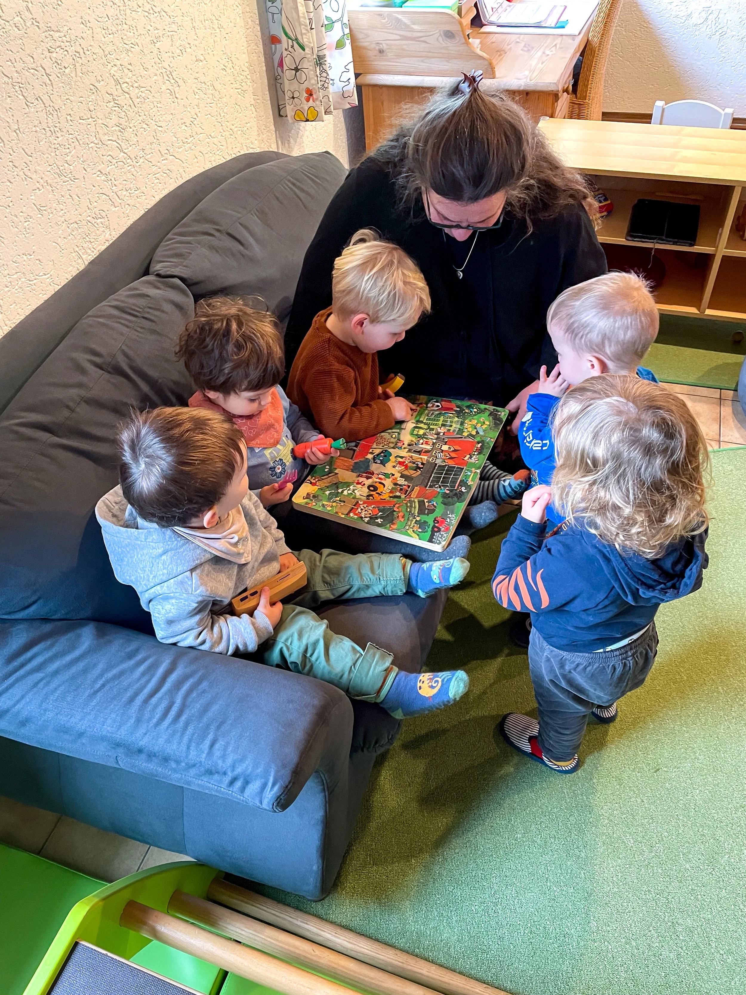 Tagesmutter verbringt Zeit gemeinsame Zeit mit den Kindern. Sie lesen ein Wimmelbuch.