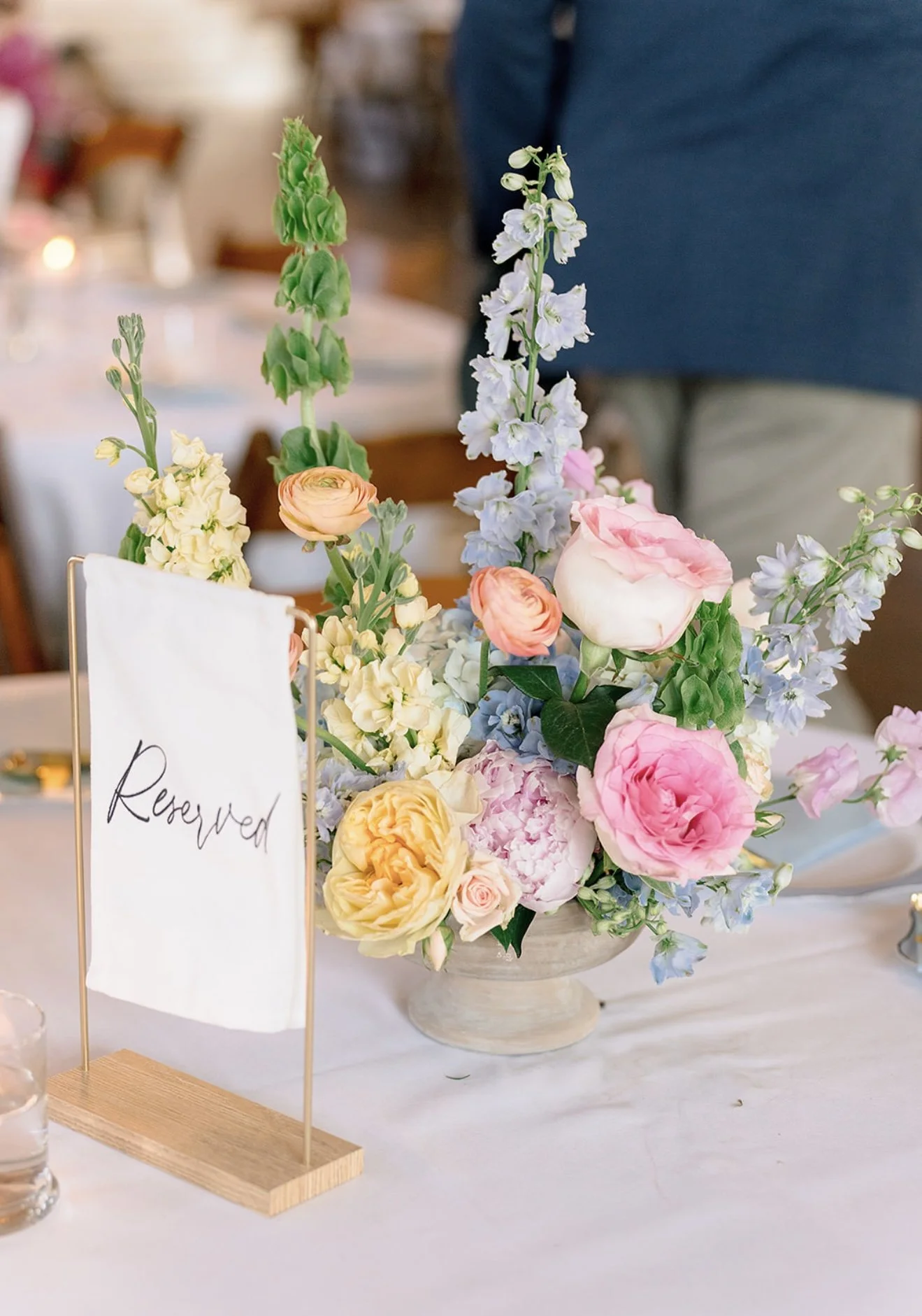 A floral centerpiece with pink, white, peach, and pale yellow flowers on a table, with a partially visible 'Reserved' sign.