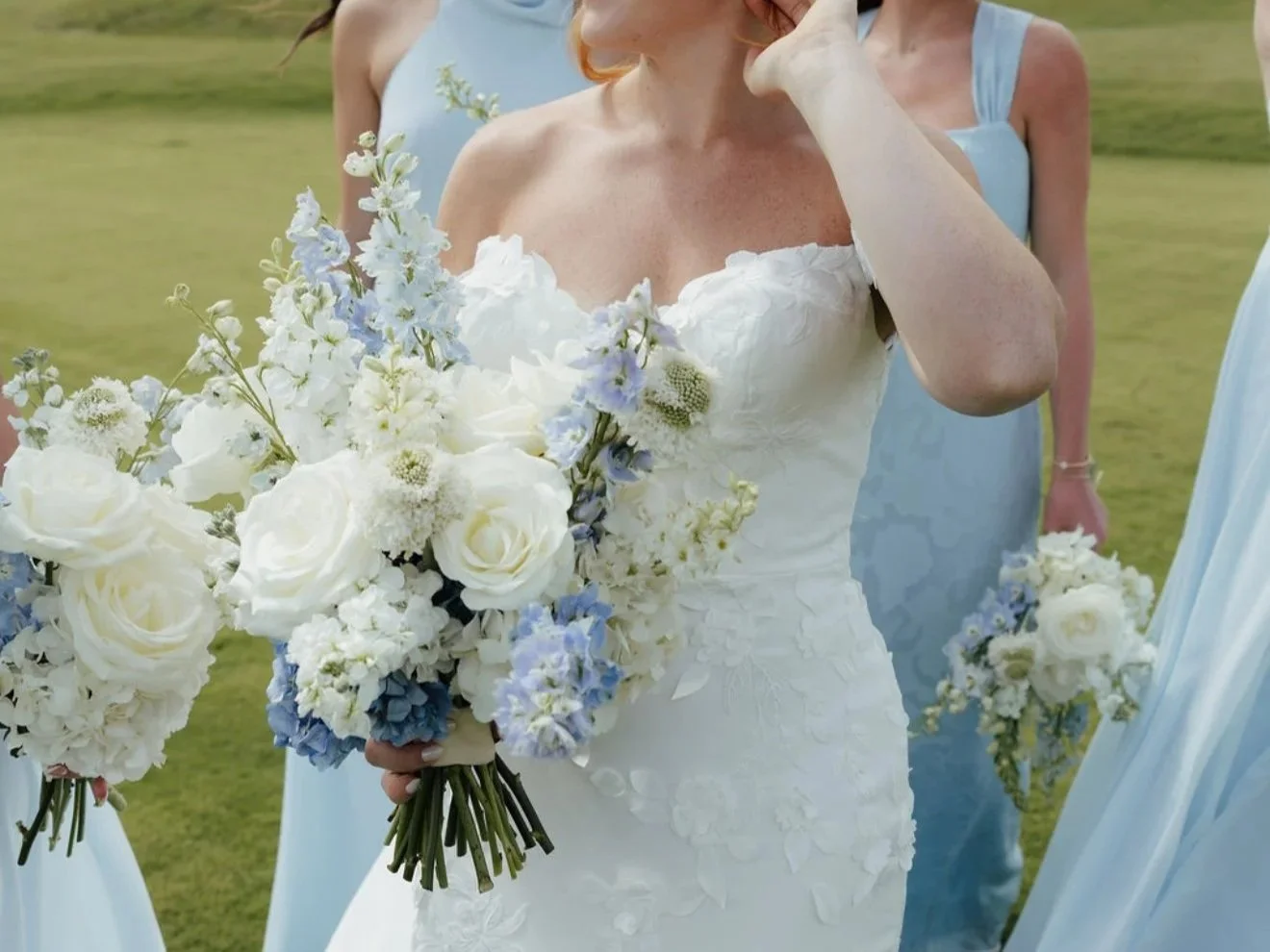 A bride holding a bouquet of white and light blue flowers at an outdoor wedding.