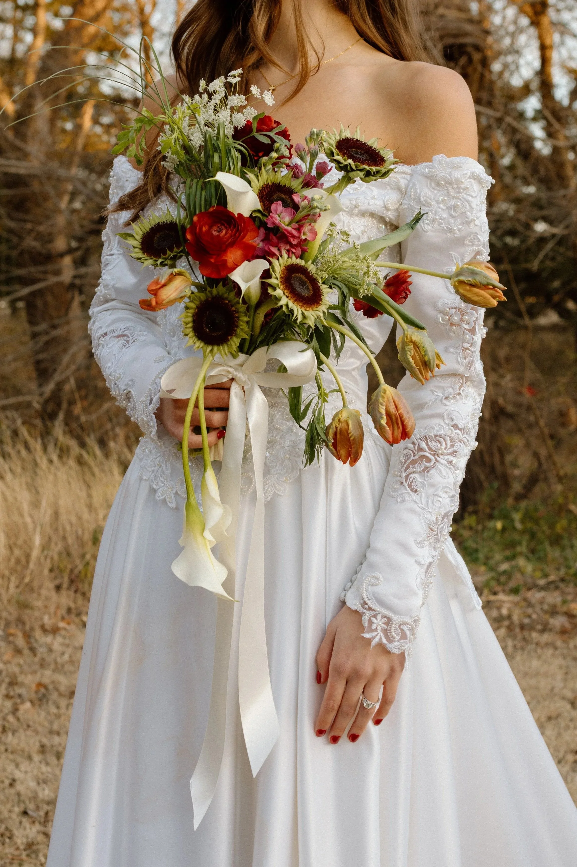 A woman in a white lace wedding dress holding a bouquet of flowers outdoors.