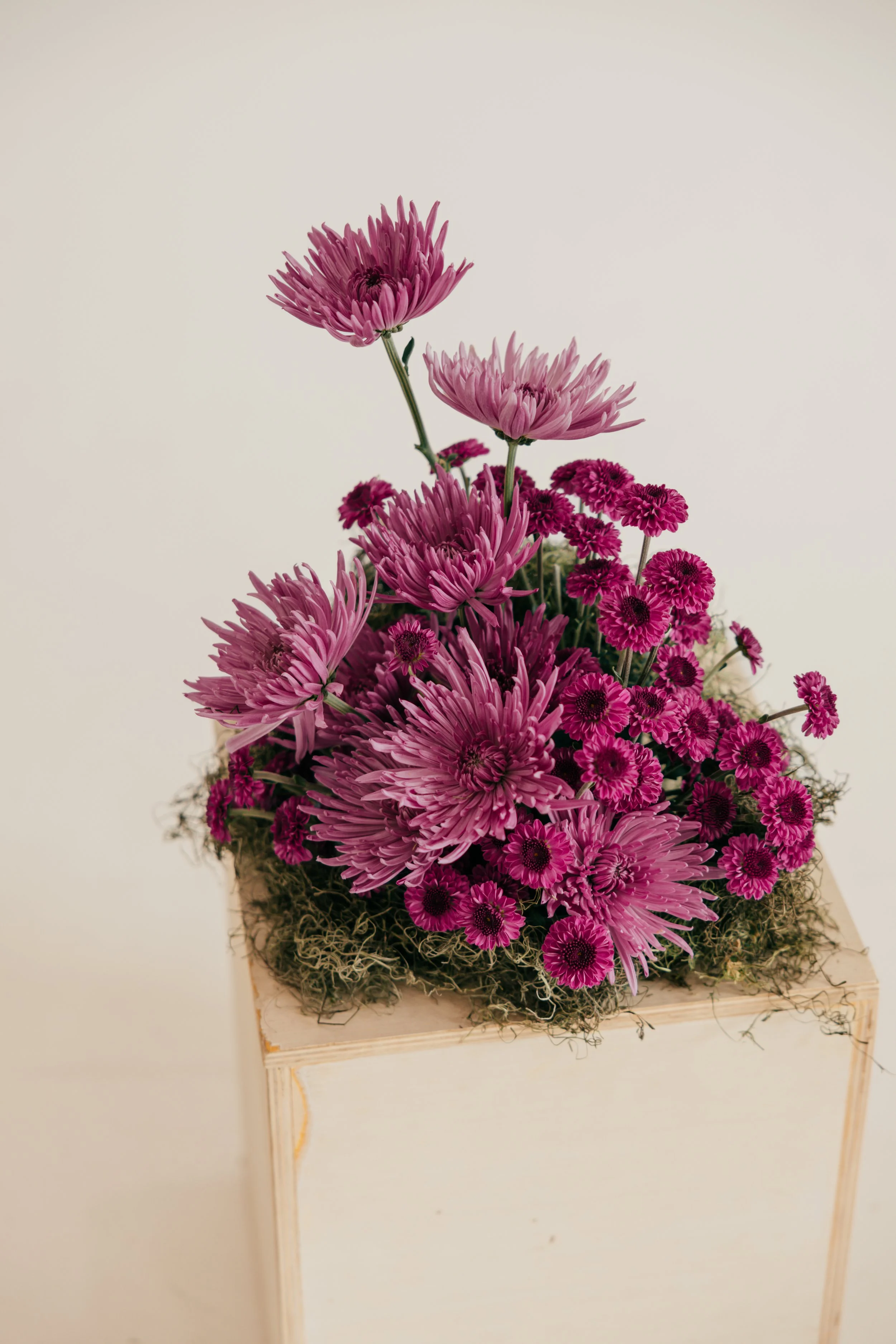 Pink and purple chrysanthemums and daisies in a flower arrangement on a wooden stand.