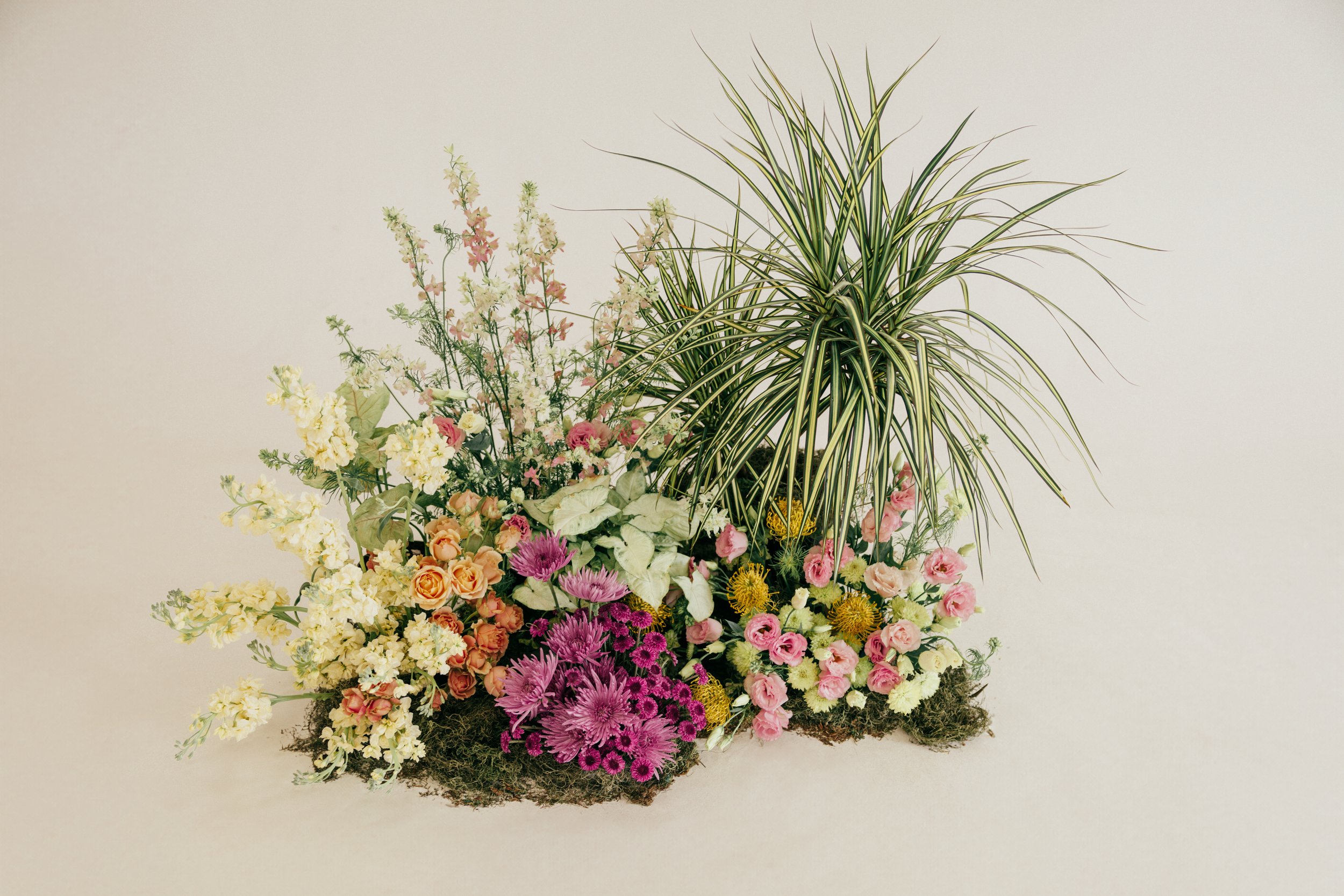 Arrangement of mixed colorful flowers and green foliage on a plain background.