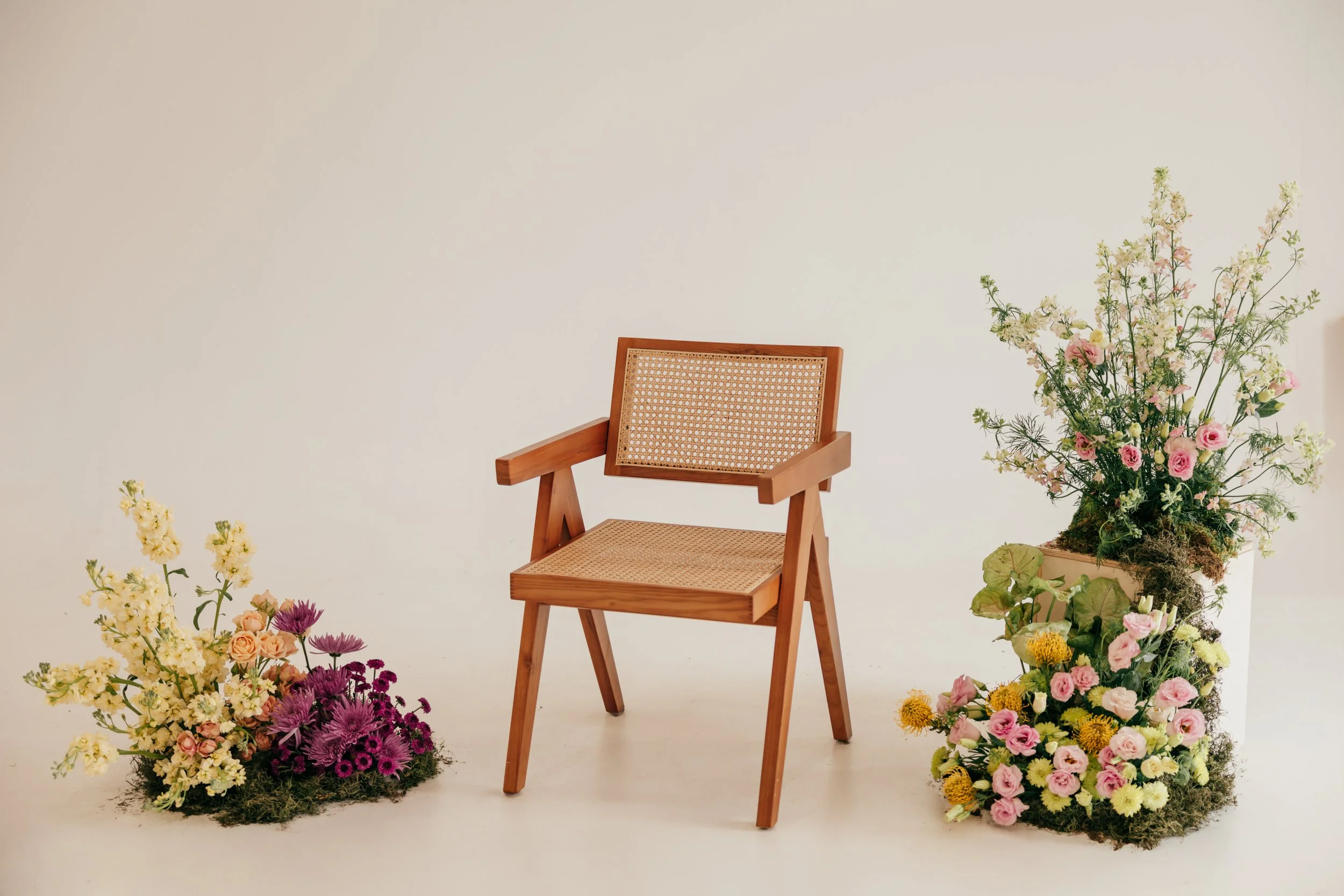 Wooden chair with woven seat and backrest, positioned between two floral arrangements of colorful flowers in vases.
