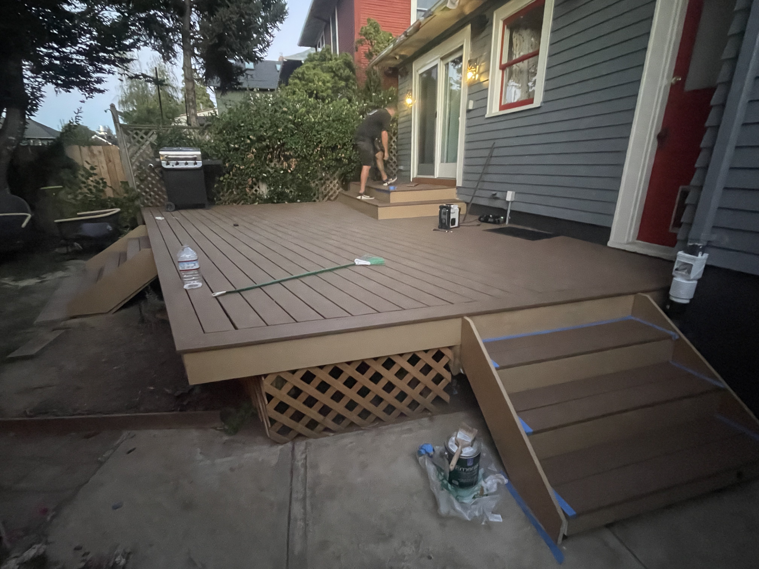A person working on building or finishing a wooden deck attached to a house, with tools and supplies nearby, in a residential backyard.