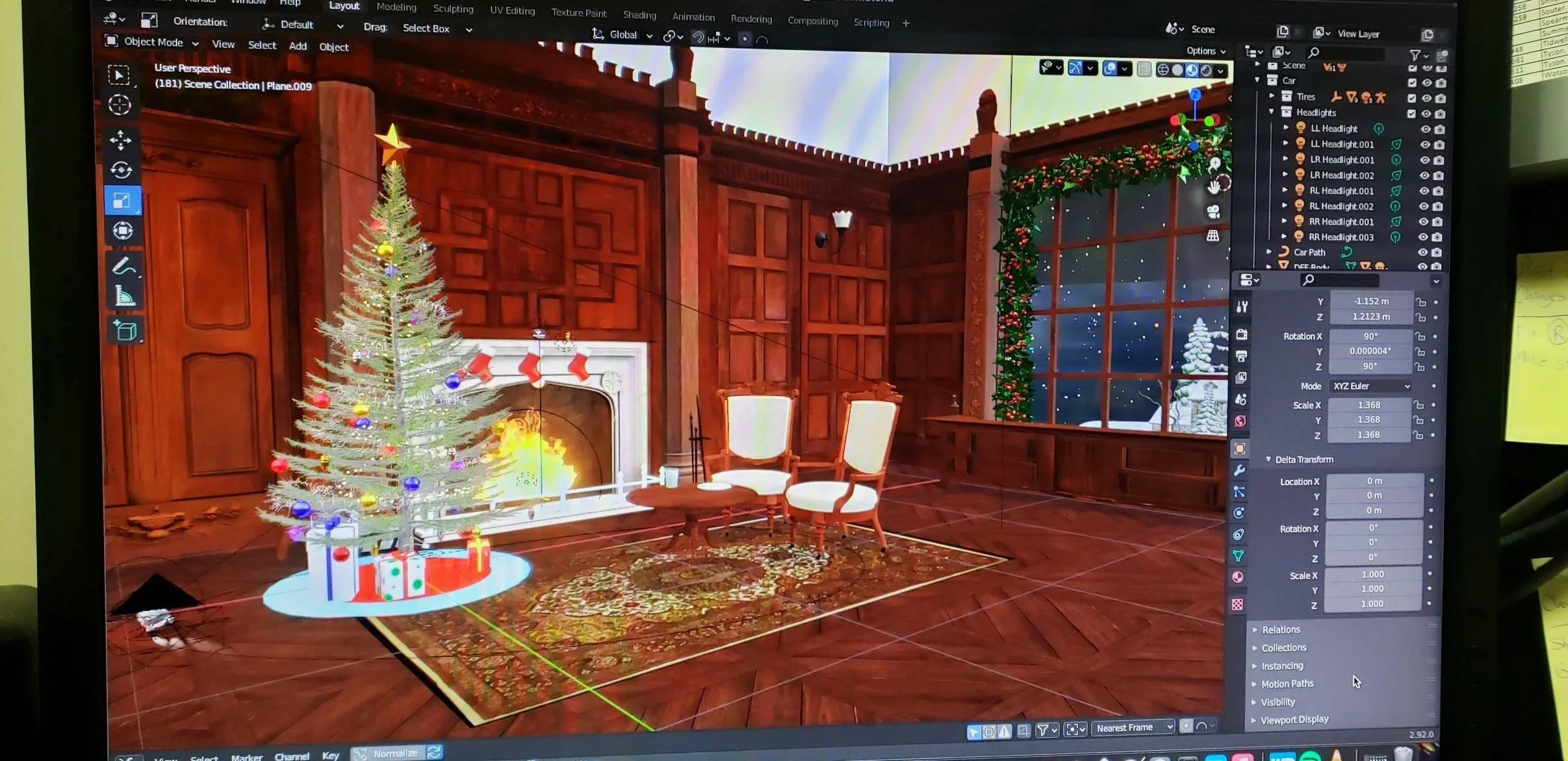 Computer screen displaying a 3D rendered scene of a cozy, wood-paneled room with a decorated Christmas tree, a fireplace with stockings, two chairs and a small table, a window showing a snowy outdoor scene, and various editing tools visible on the screen.