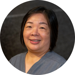 Circular profile image of a Vancouver Prosthetics & Orthotics employee, a smiling Asian woman with shoulder-length black hair, wearing a gray top, against a dark background in Vancouver, BC.