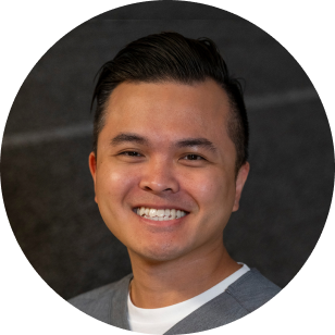 A circular profile image of a Vancouver Prosthetics & Orthotics employee, smiling man with dark hair and a gray shirt standing in front of a dark background, in Vancouver, BC.