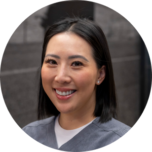 A Vancouver Prosthetics & Orthotics employee, asian woman with shoulder-length black hair smiling against a dark background, wearing a gray top in Vancouver, BC.