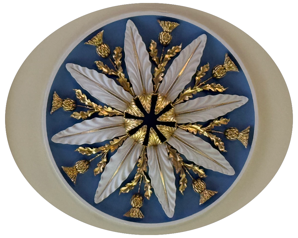 A decorative ceiling medallion with gold and white ornaments resembling feathers and floral elements, arranged in a radial pattern.