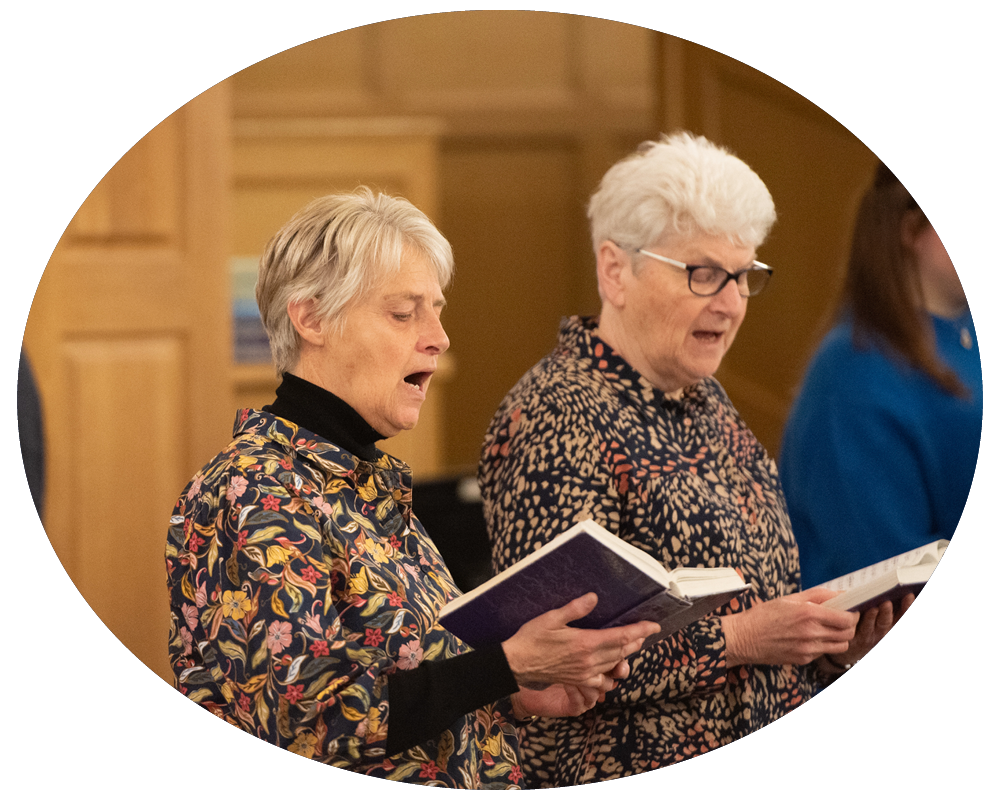Two elderly women singing from hymn books during a church service.