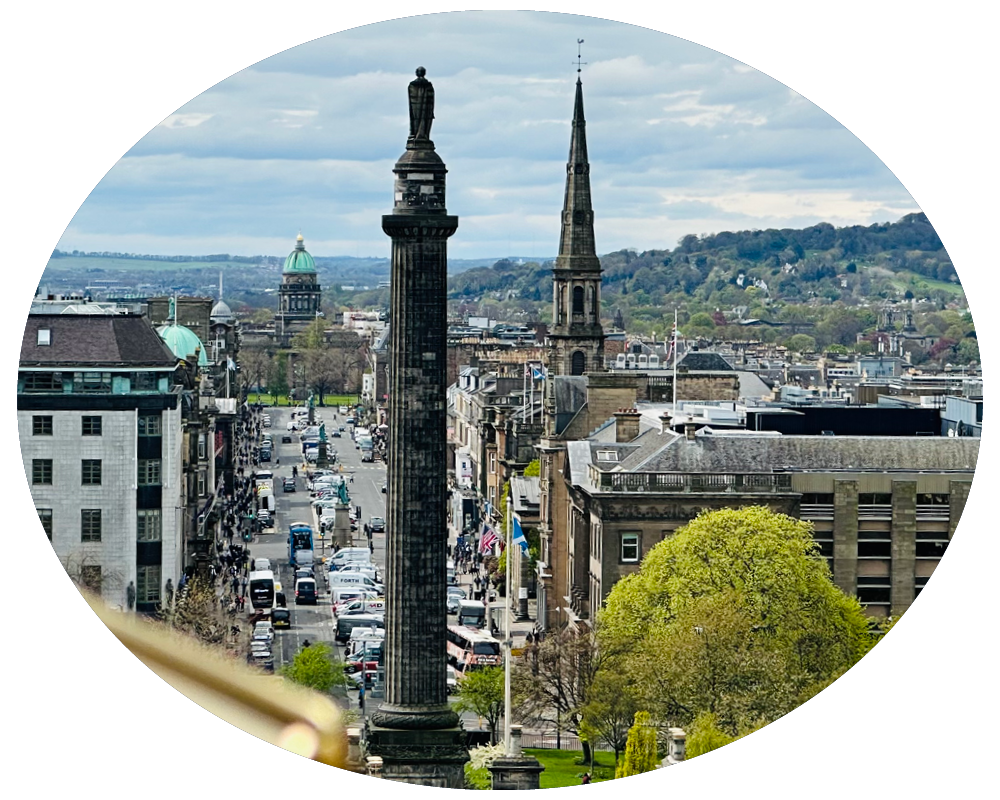 Panoramic view of a city street with historical buildings, a tall column monument, and a church steeple, with hills in the background.