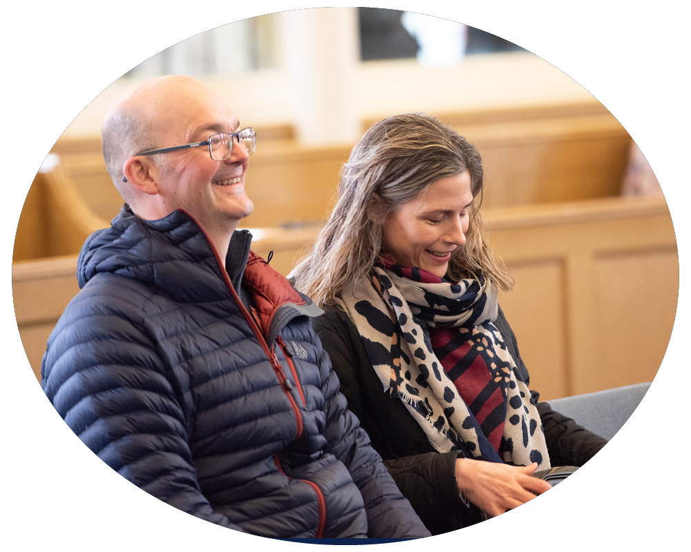 A man and woman sitting in a church, smiling and looking down.
