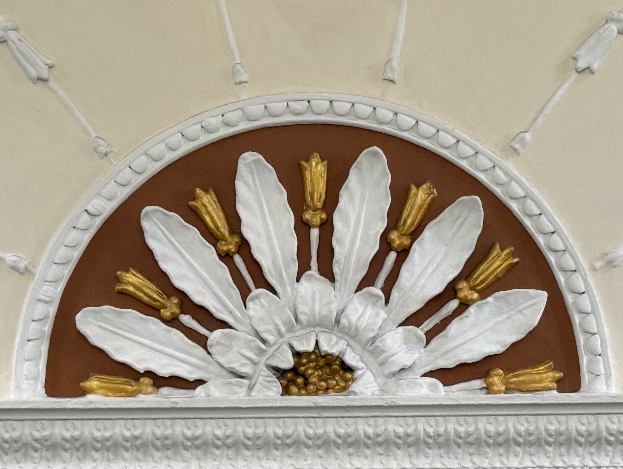 Close-up of a decorative wall clock with a floral motif featuring white petals and gold accents on a brown background.