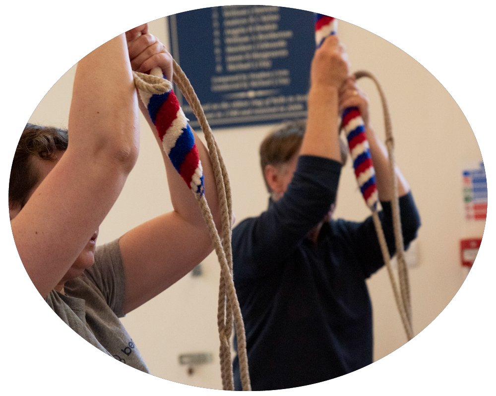 People raising ropes with red, white, and blue striped covers in an indoor setting.