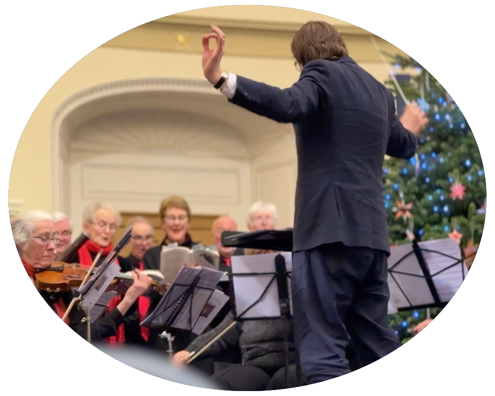 Orchestra conductor leading a choir during a Christmas concert with a decorated Christmas tree in the background.