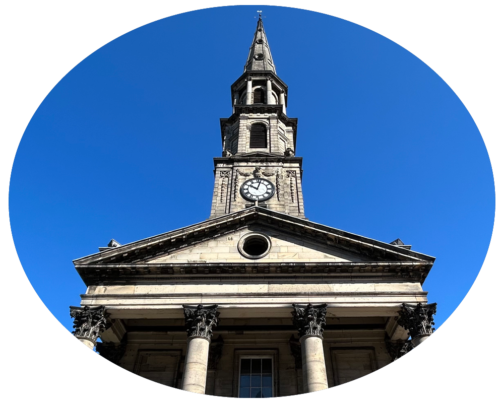Front view of a historic church with a clock tower, stone columns, and a triangular pediment, clear blue sky background.
