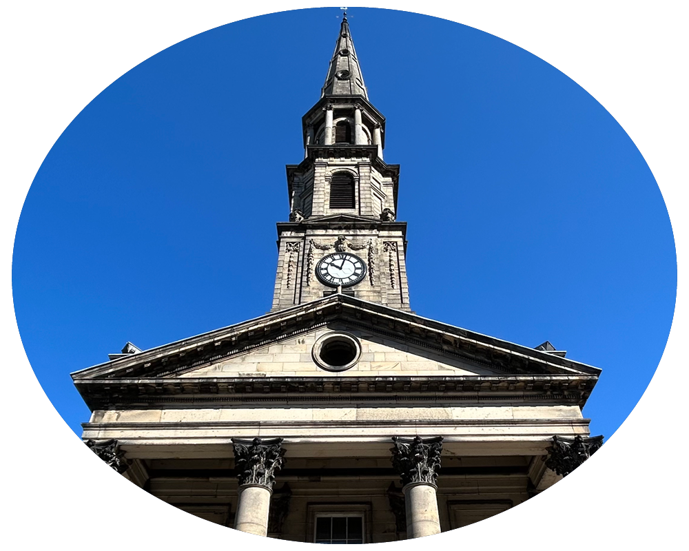 A historic stone church with a tall steeple and clock, viewed from below against a clear blue sky.