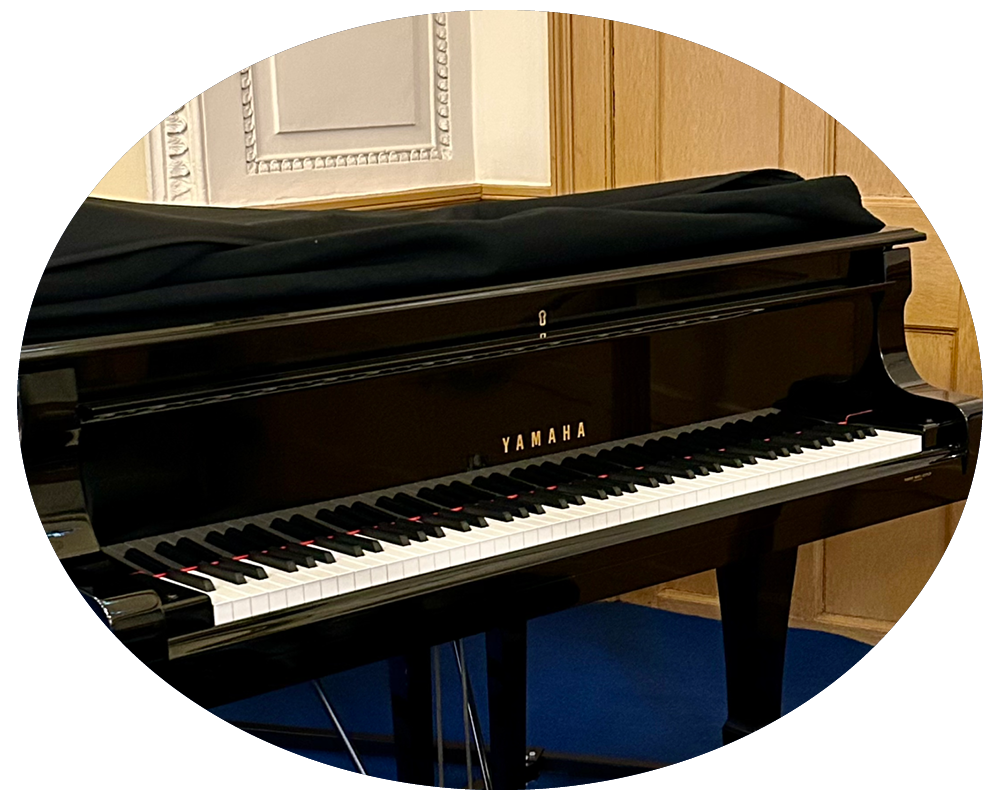 A black Yamaha grand piano with a closed lid, situated in a room with wood-paneled walls and a decorative wall panel.