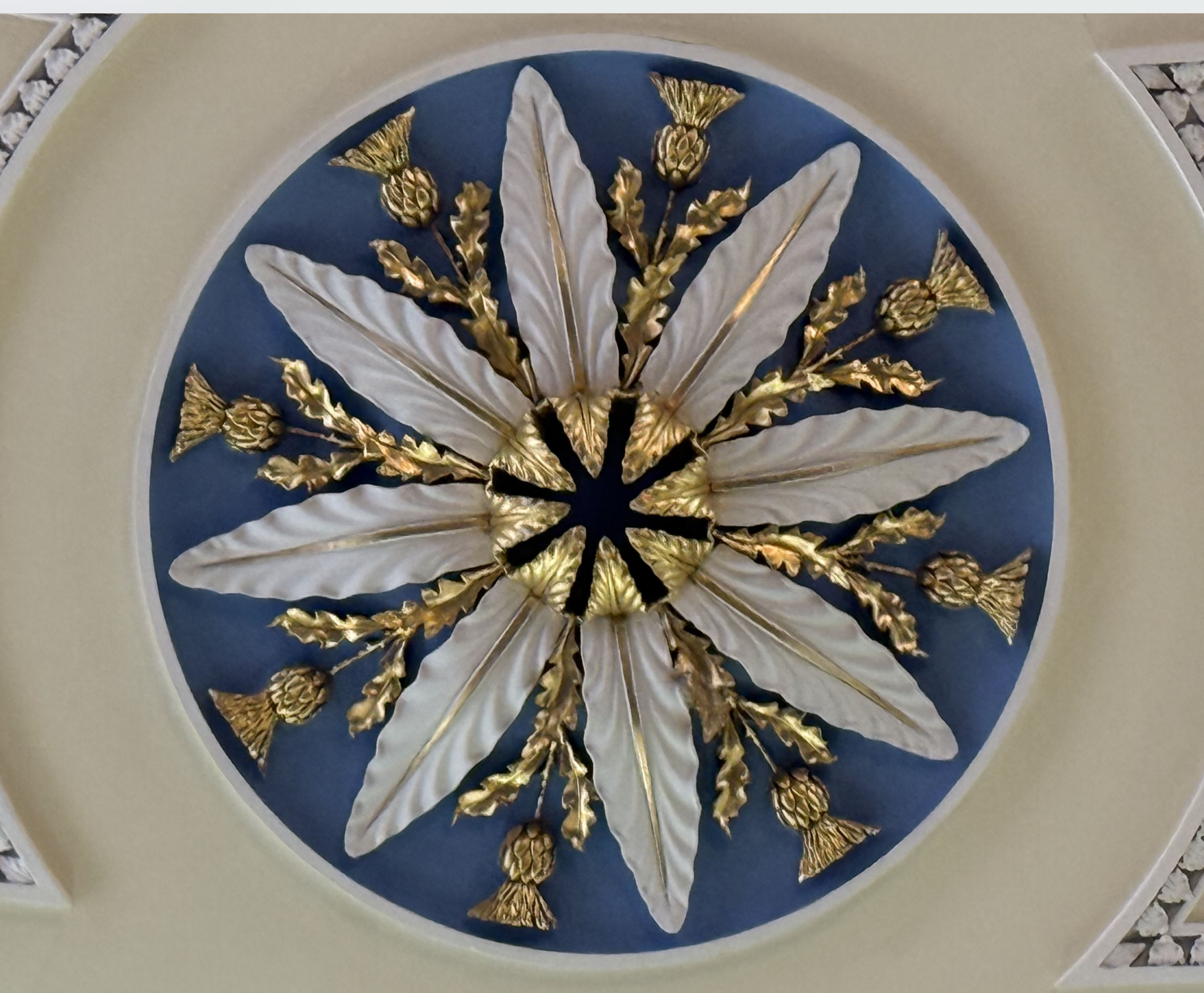 Decorative wall with golden flowers and white leaves set against a blue circular background, edged by a white arch.