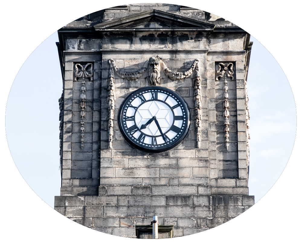 A close-up of a historic clock tower with Roman numerals and an ornate face on a stone building.